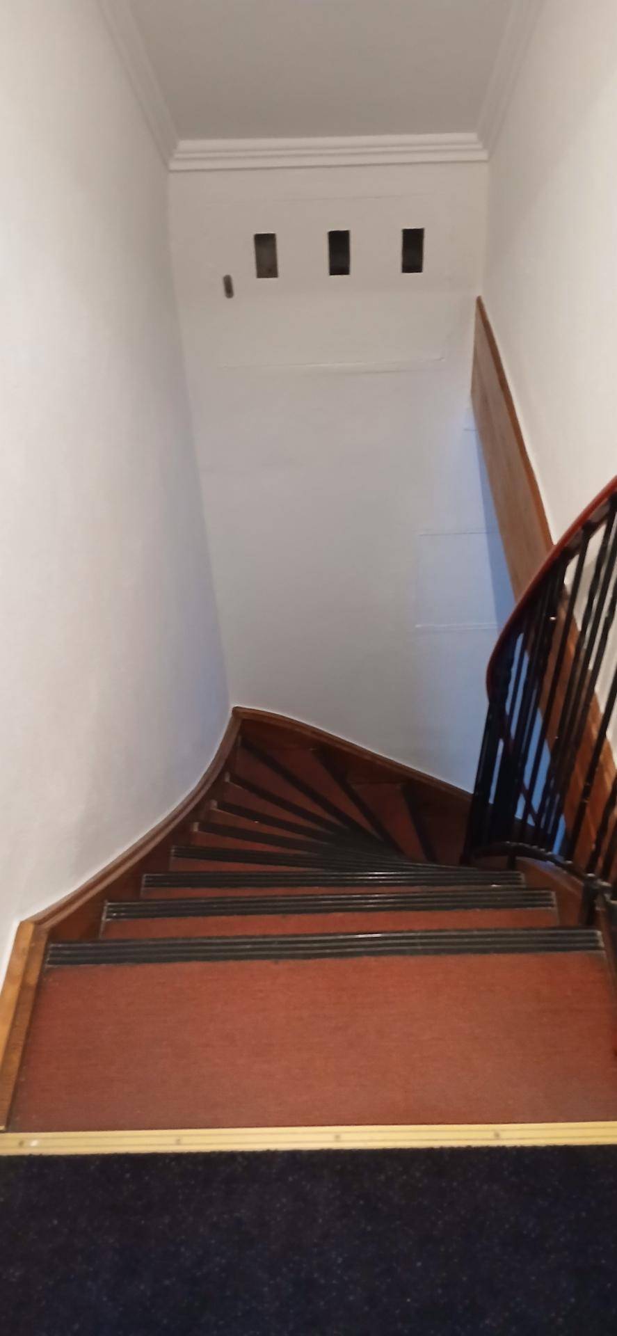Elegante Holztreppe mit dunklem Teppich und geschwungenem Geländer führt in die obere Etage.