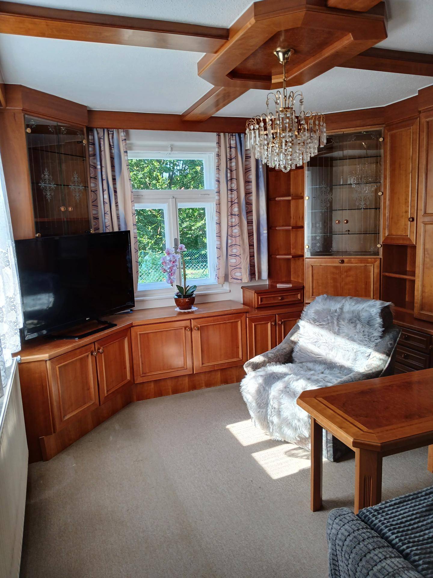 Gemütliches Wohnzimmer mit Holzvertäfelung, Teppichboden und einem Kronleuchter an der Decke.