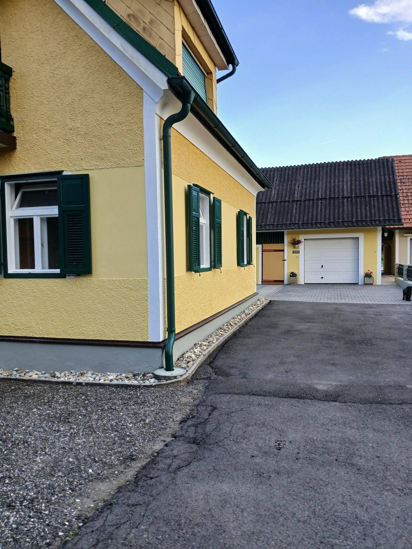 Seitenansicht des Hauses mit grünen Fensterläden und einer Garage im Hintergrund auf dem Grundstück.