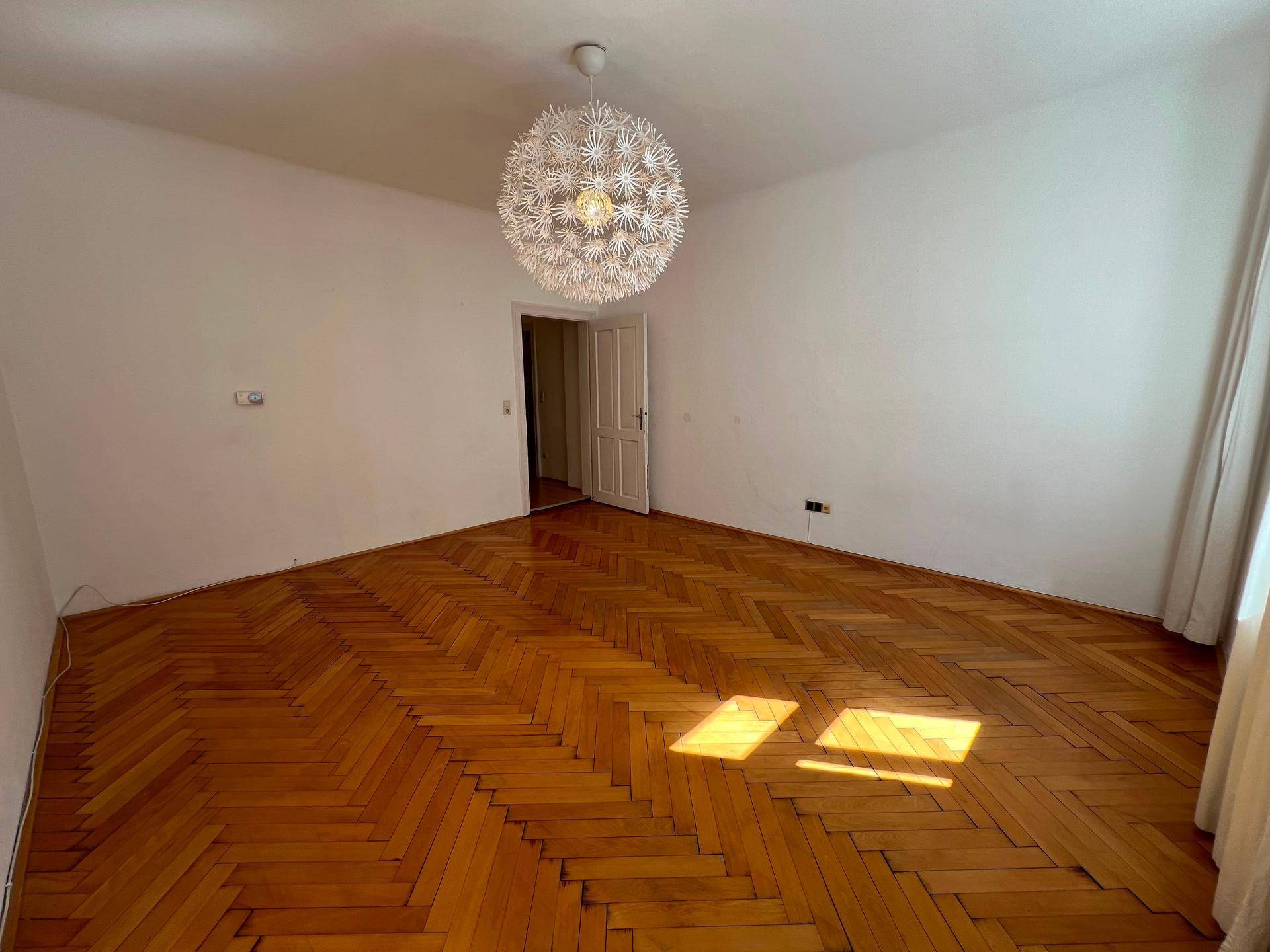 Helles Wohnzimmer mit klassischem Fischgrätparkett und Zugang zu weiteren Räumen.