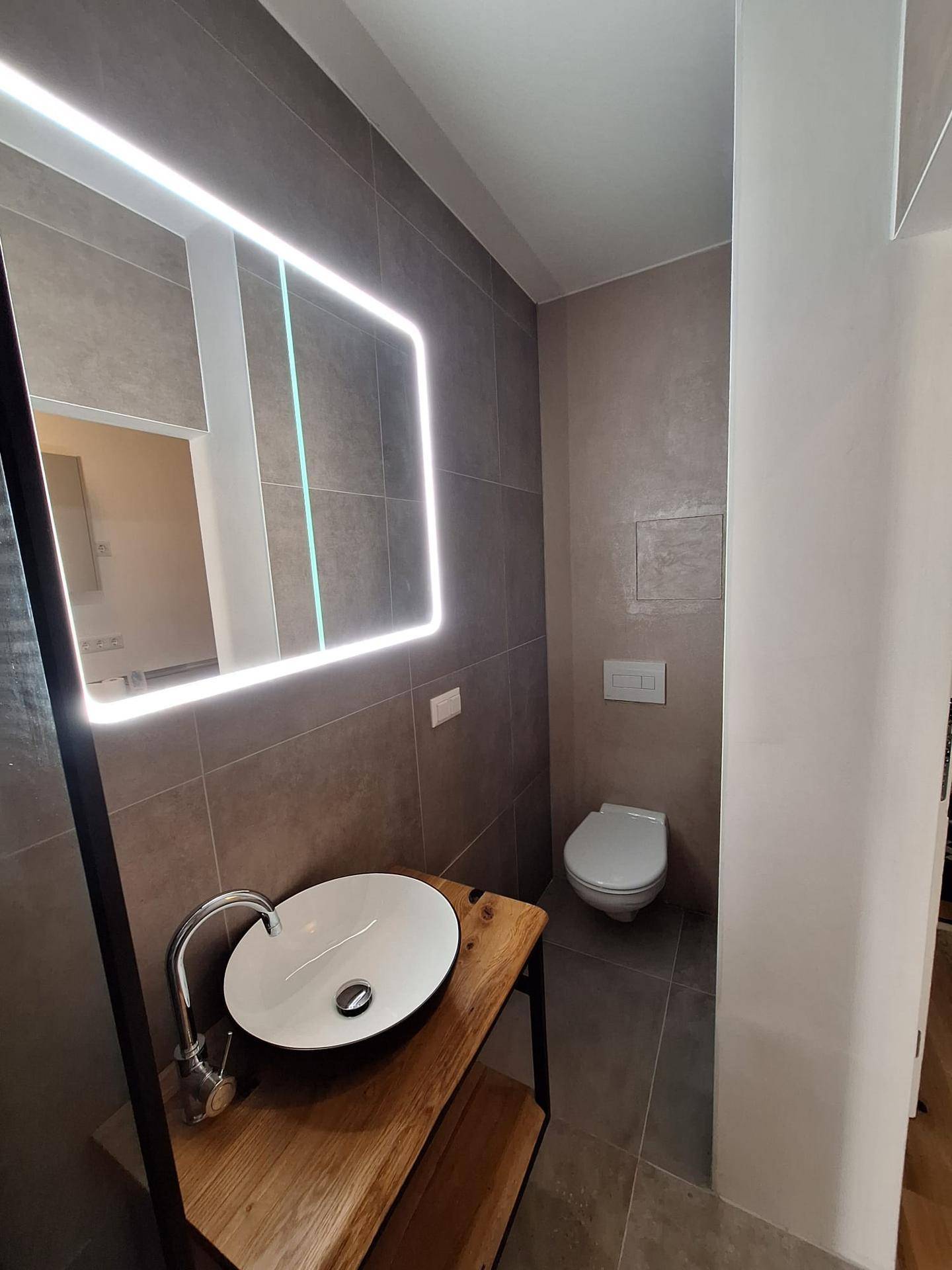 Modernes Badezimmer mit Aufsatzwaschbecken auf Holzplatte und beleuchtetem Spiegel.