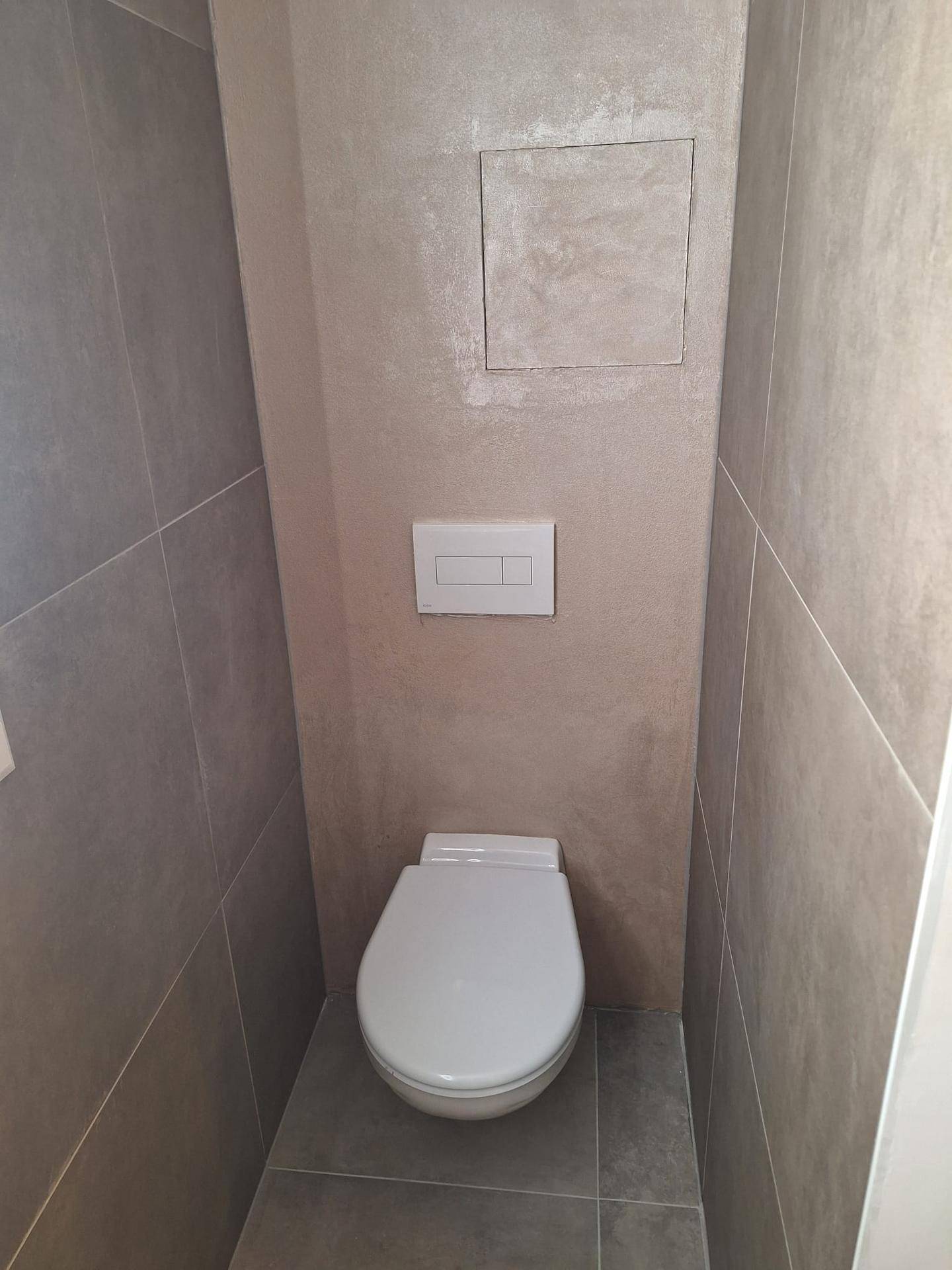 Modernes separates WC mit Wand-WC und grauen Großformatfliesen.
