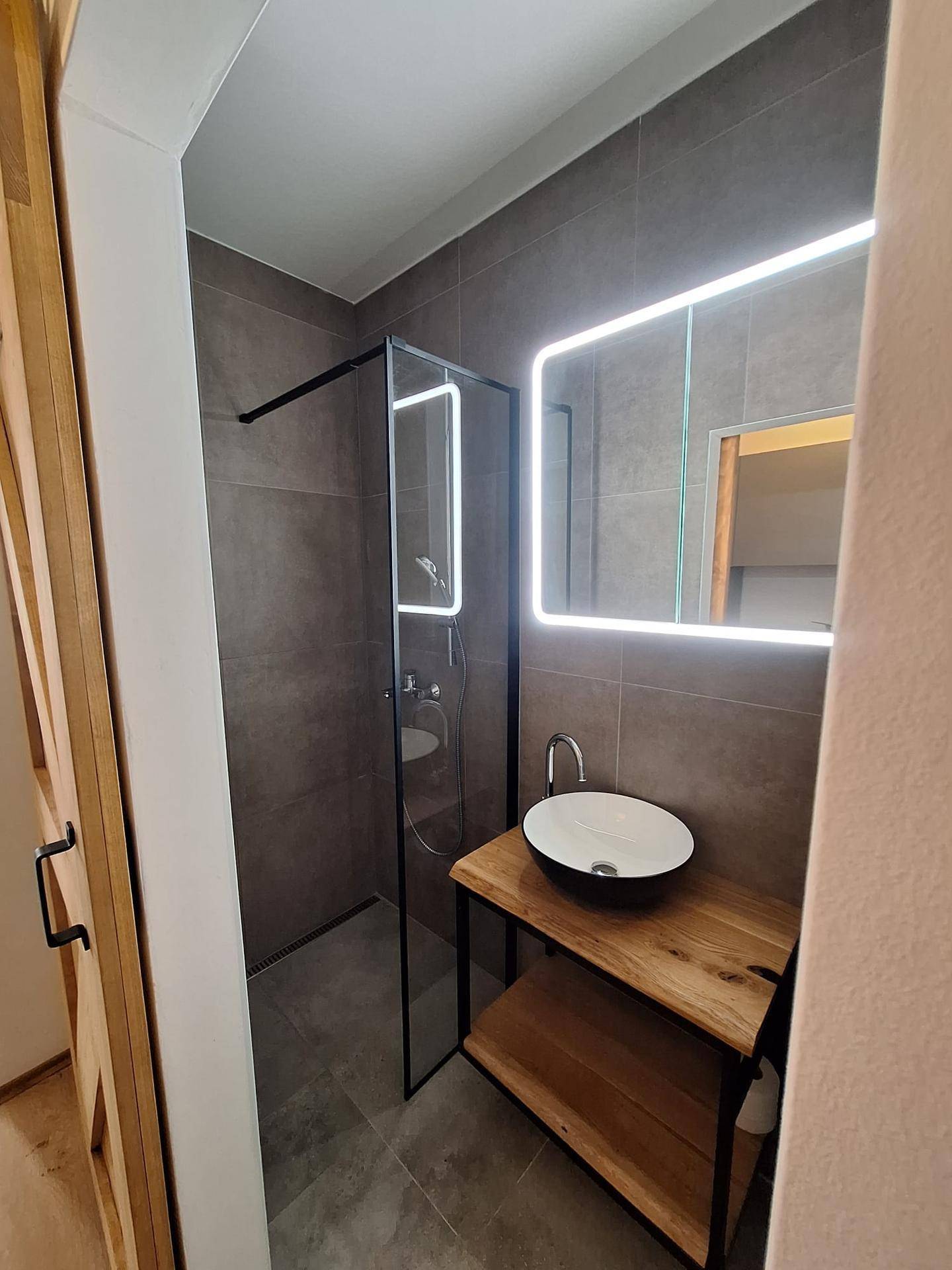 Modernes Badezimmer mit ebenerdiger Dusche, Aufsatzwaschbecken und beleuchtetem Spiegel.