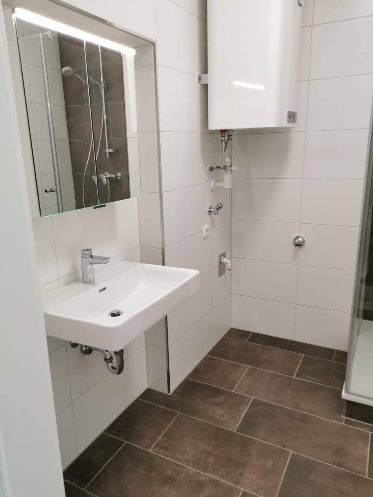 Badezimmer mit modernem Waschbecken, beleuchtetem Spiegelschrank und Duschbereich.