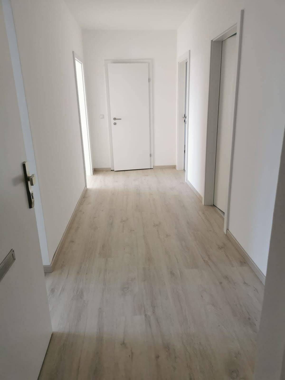 Heller Flur mit Laminatboden und weißen Wänden, der zu verschiedenen Räumen führt.