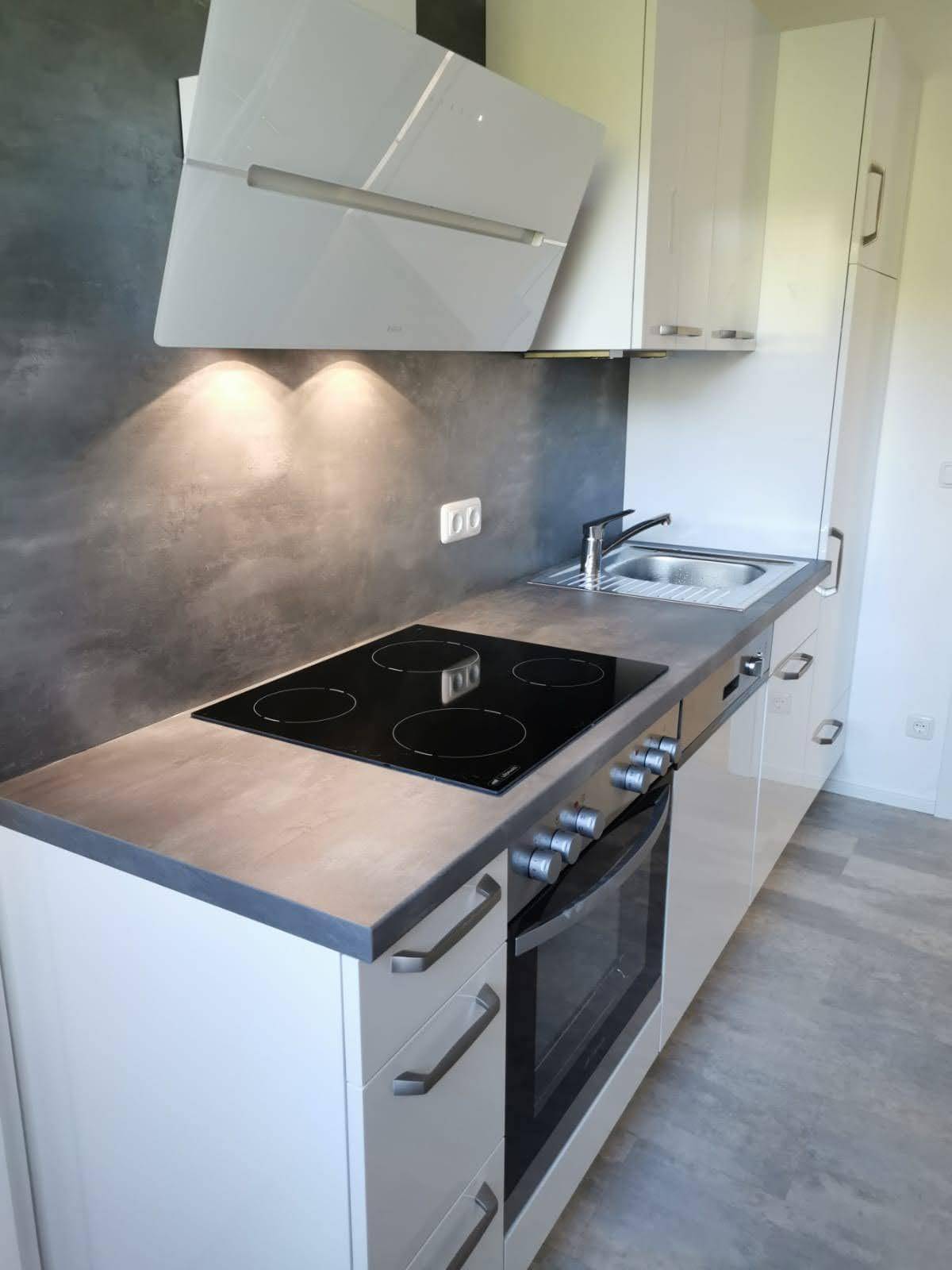 Moderne Einbauküche mit weißen Hochglanzfronten, Induktionskochfeld und Dunstabzugshaube.
