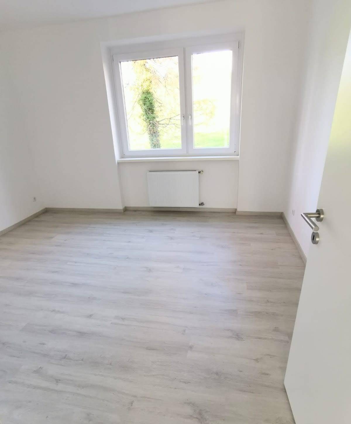 Helles Zimmer mit Laminatboden und Blick ins Grüne, ideal als Schlaf- oder Arbeitszimmer.