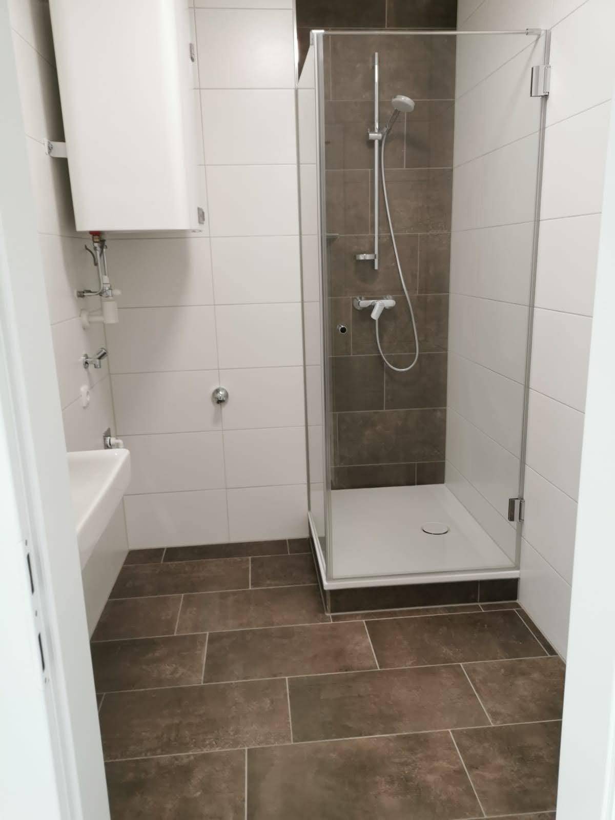 Modernes Badezimmer mit Duschkabine, weißen Wandfliesen und dunklem Fliesenboden.