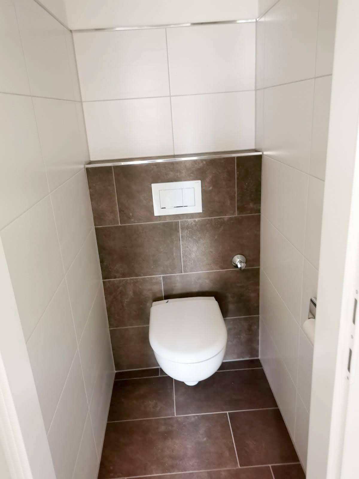 Separates WC mit wandhängender Toilette und modernen Fliesen in Weiß und Dunkelgrau.