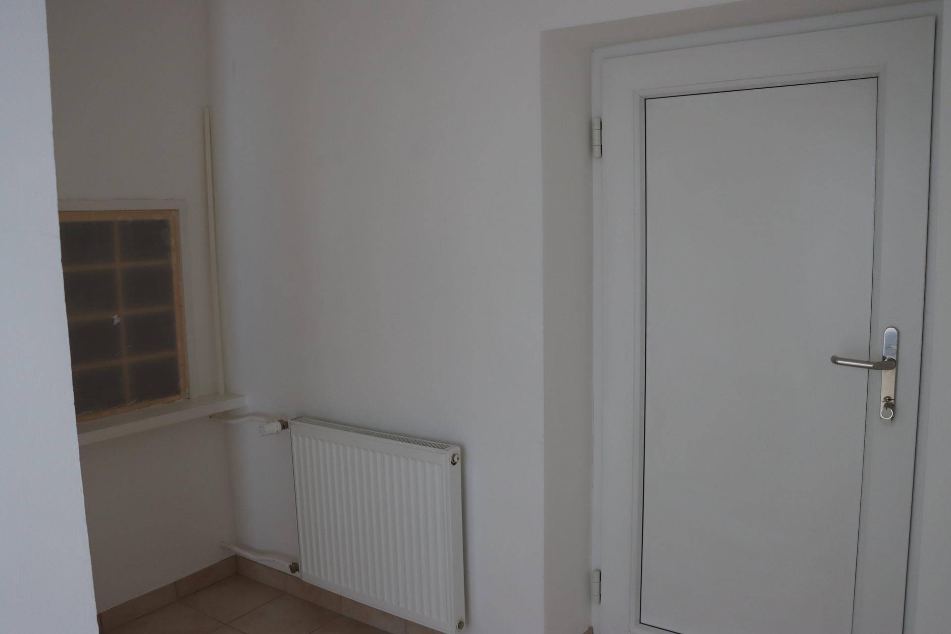 Eingangsbereich mit weißer Tür, Heizkörper und einem kleinen Fenster mit Glasbausteinen für Licht.