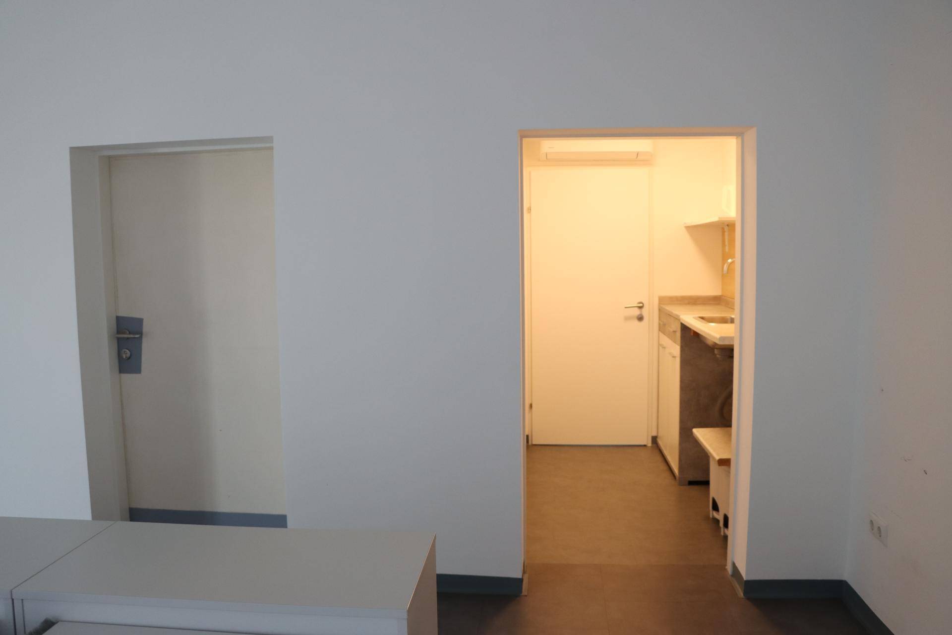 Heller Flur mit weißer Tür und Blick in eine kleine Küchenzeile mit Spüle und Arbeitsplatte.