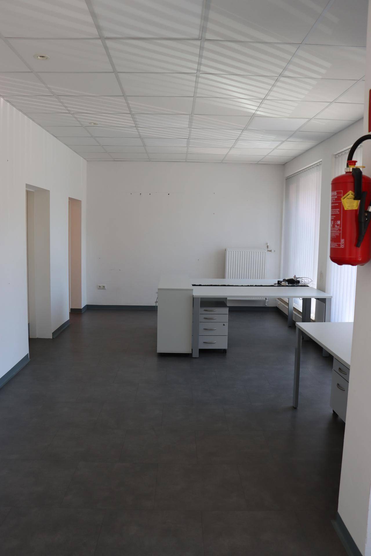 Geräumiges, leeres Büro mit dunklem Vinylboden, weißen Wänden und einer abgehängten Decke.