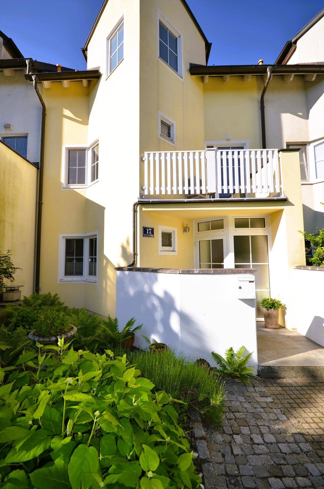 Gelbe Fassade mit weißen Fenstern, kleinem Balkon und einem gepflegten Vorgartenbereich.
