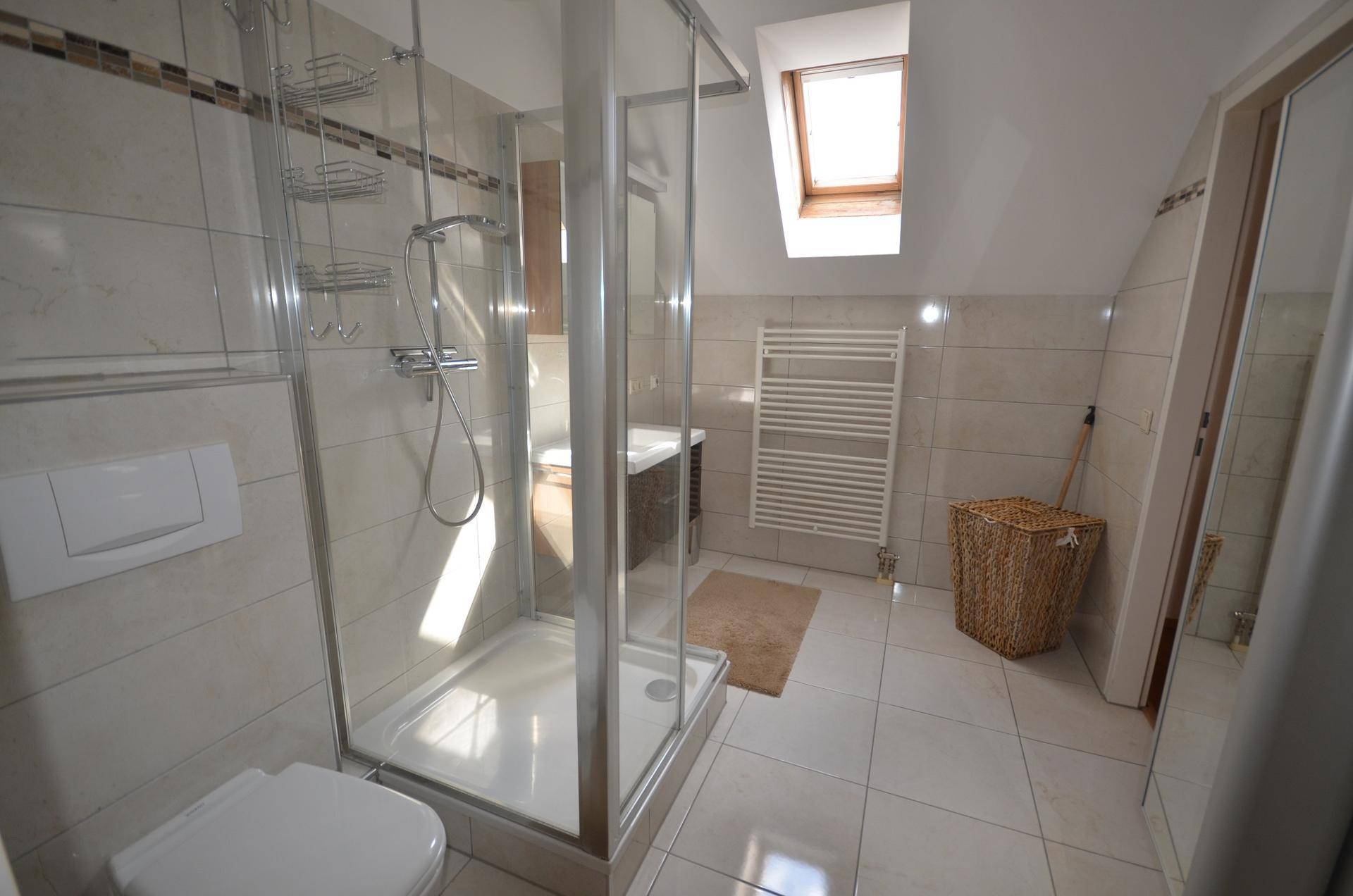 Helles Badezimmer mit Duschkabine, WC, Handtuchheizkörper und natürlichem Licht durch das Dachfenster.