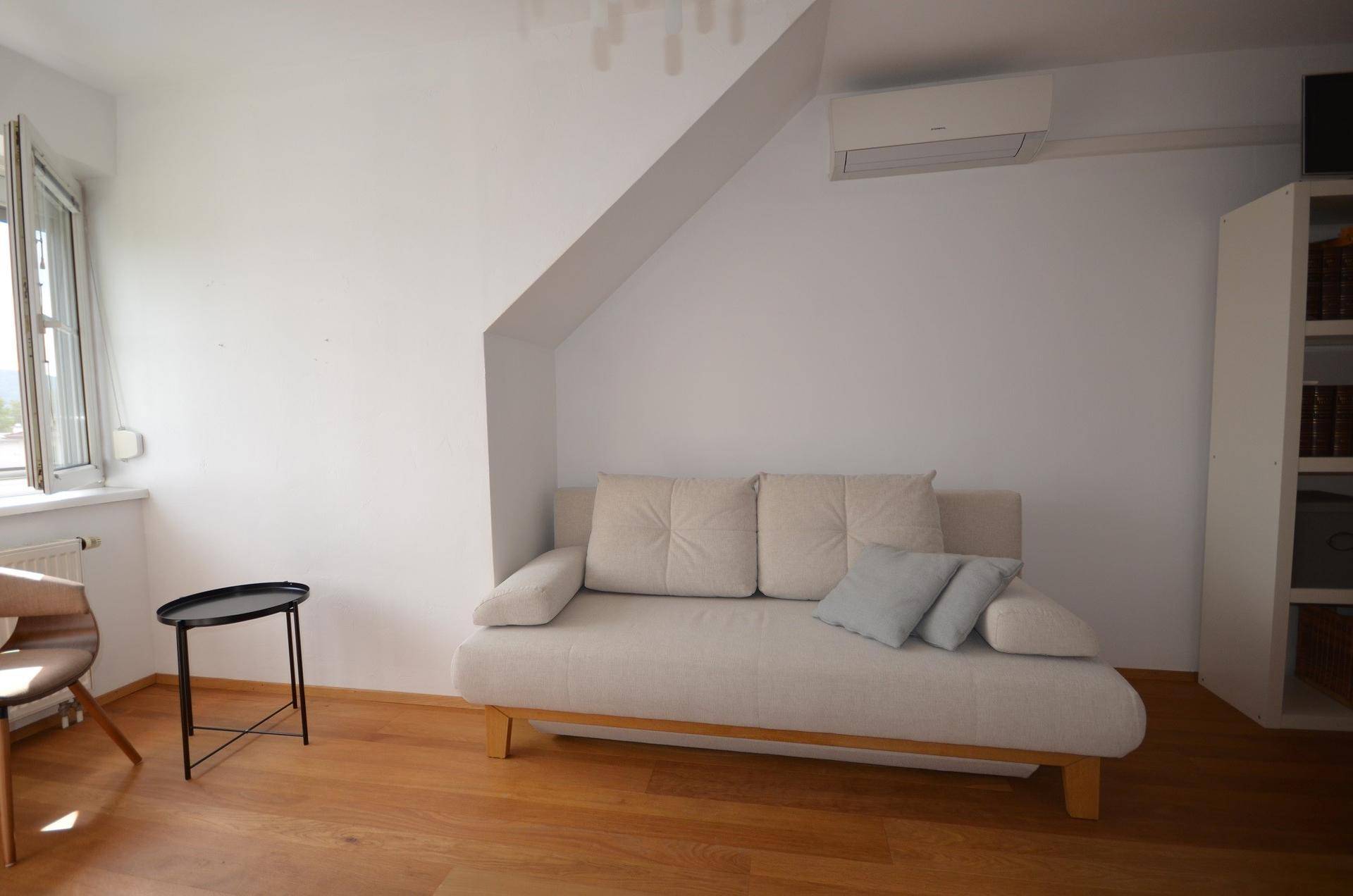 Gemütliches Zimmer mit Holzboden, Dachschräge, Sofa und Klimaanlage.