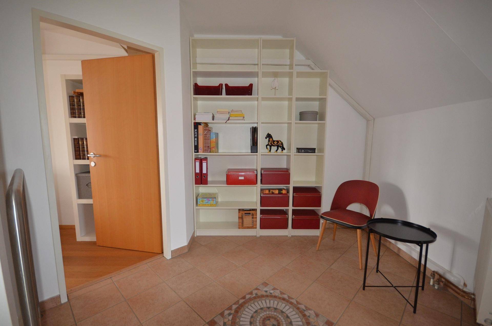 Heller Flurbereich mit Fliesenboden, großem Bücherregal und Dachschräge.