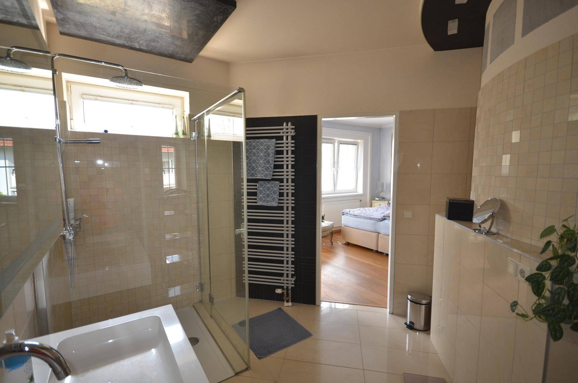Helles Badezimmer mit begehbarer Dusche, Handtuchheizkörper und Zugang zu weiteren Räumen.