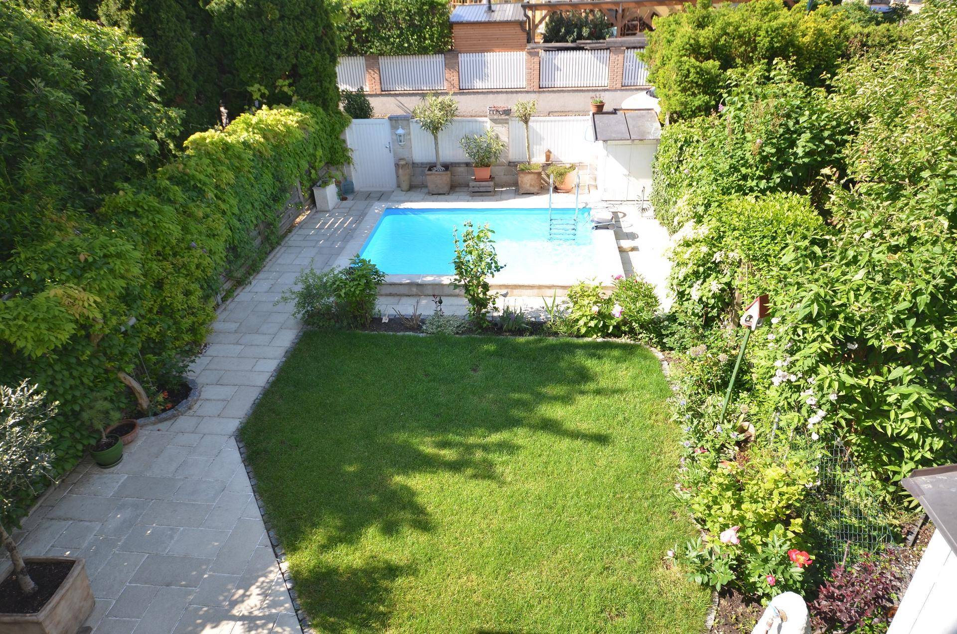 Vogelperspektive des gepflegten Gartens mit Swimmingpool, Rasenfläche und Steinweg.