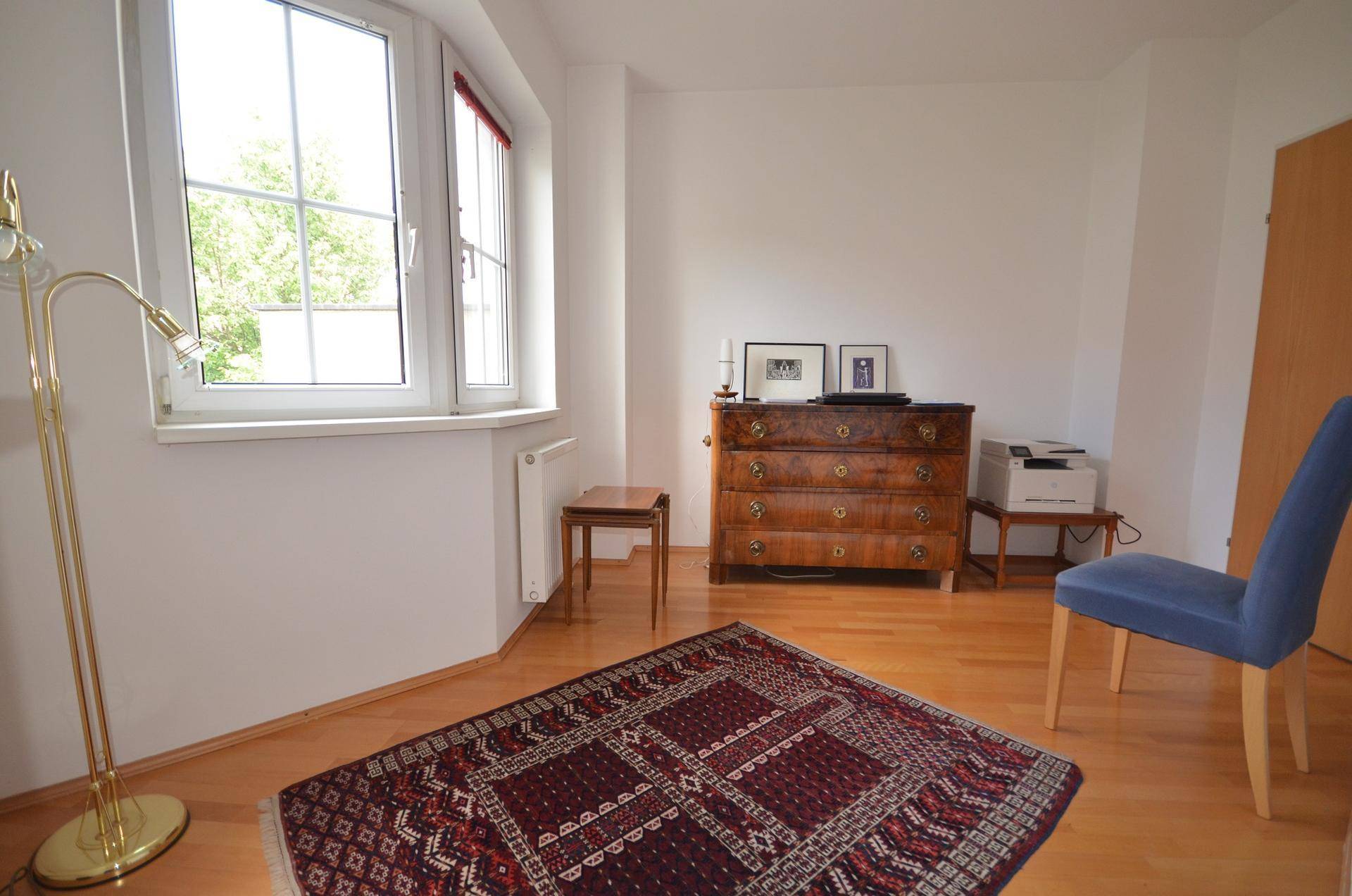 Helles Zimmer mit Holzboden, Fenster und einer klassischen Kommode.