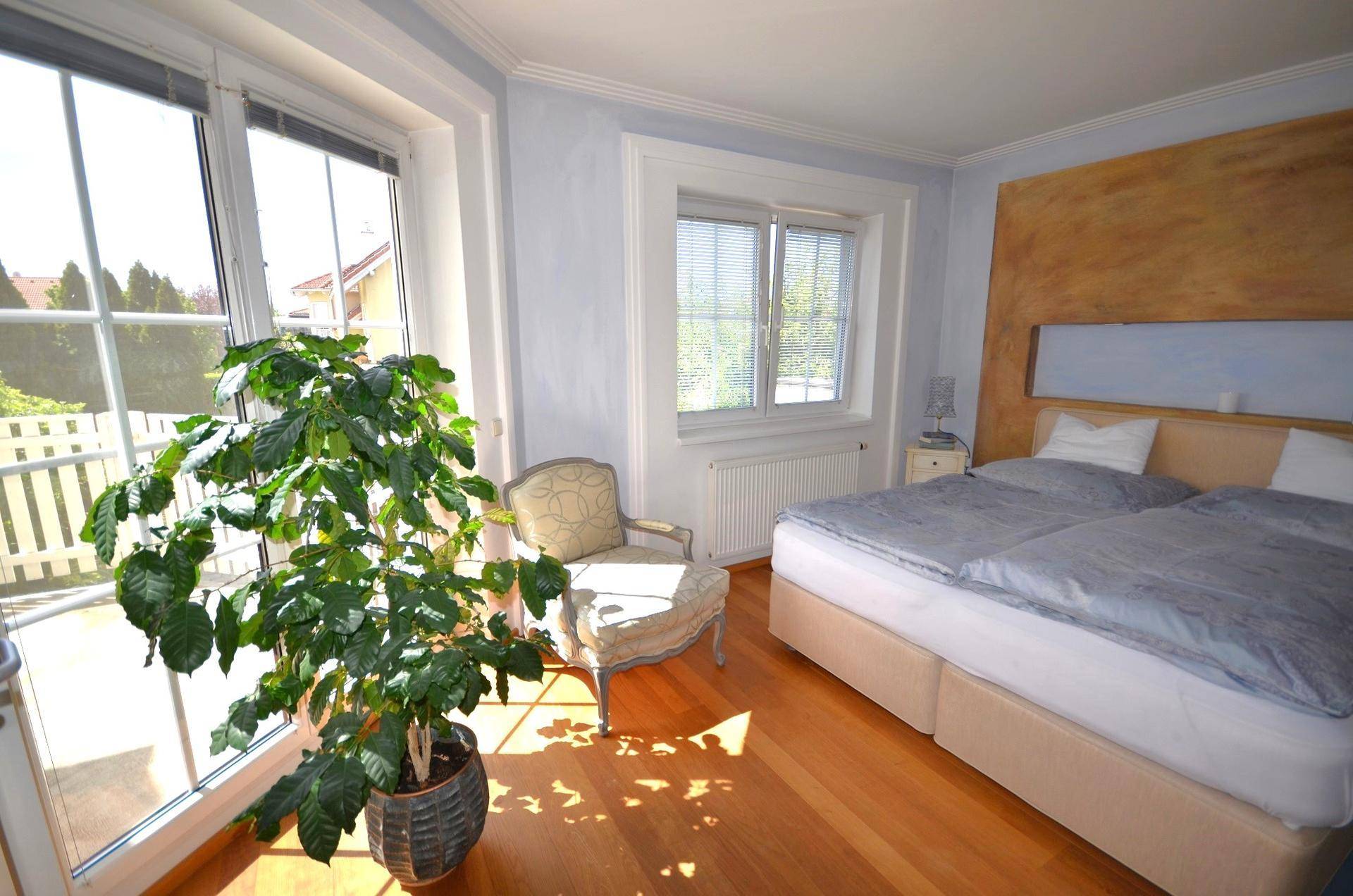 Lichtdurchflutetes Schlafzimmer mit Holzboden, großem Fenster und Zugang zum Balkon.