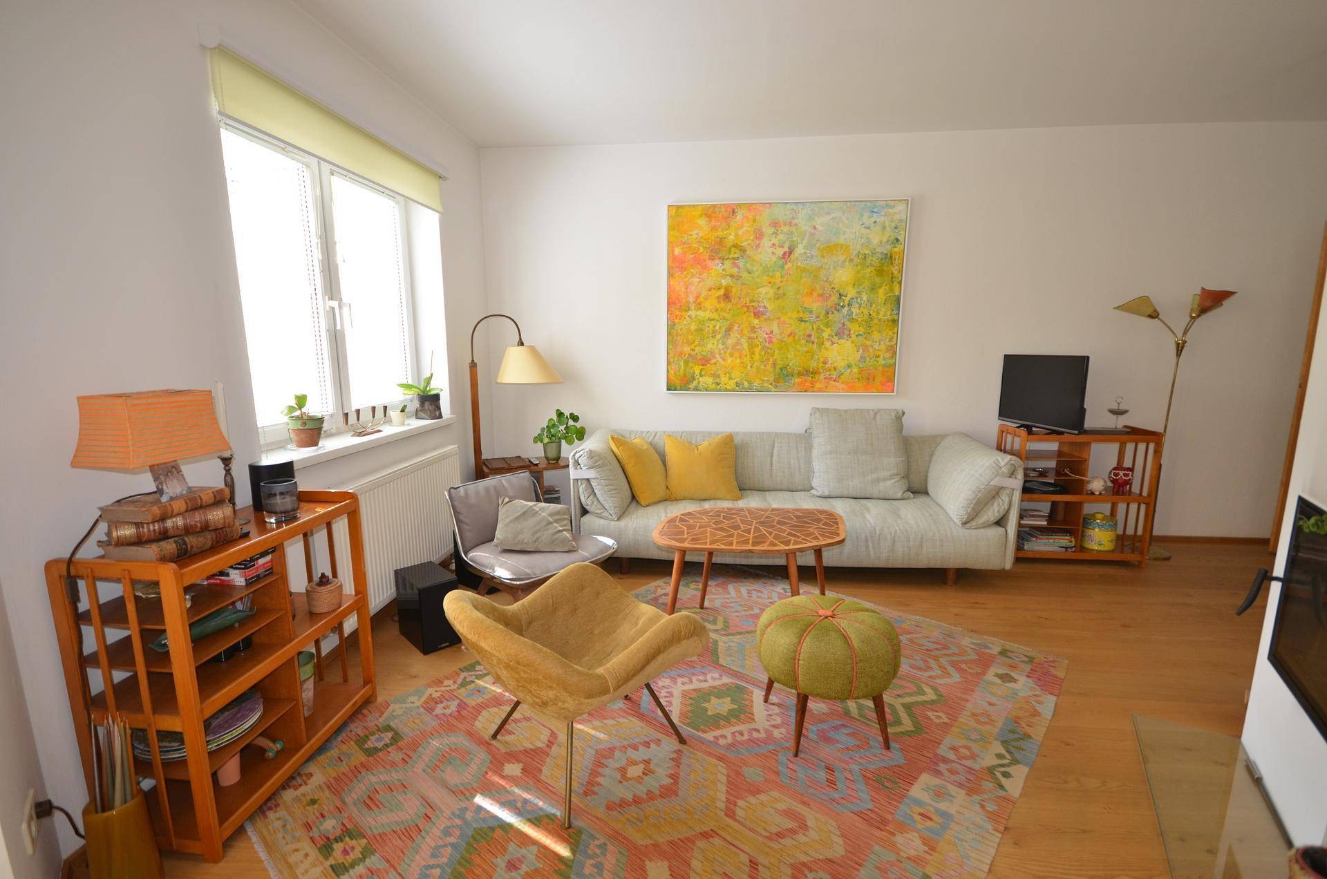 Helles Wohnzimmer mit bequemen Sitzmöbeln, farbenfrohem Teppich und einem großen Kunstwerk.