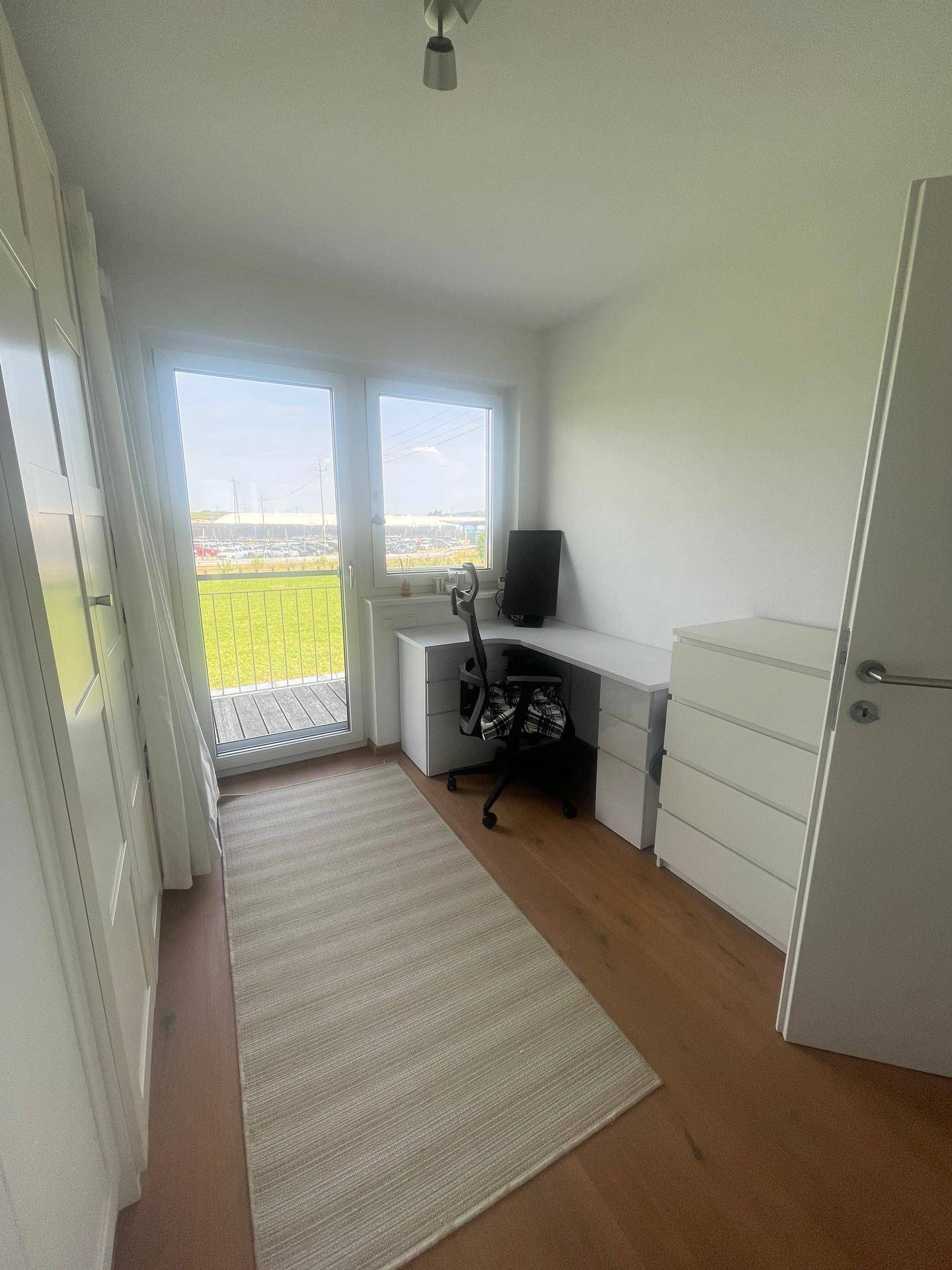Helles Arbeitszimmer mit großem Fenster, Holzboden und integrierten Schränken.