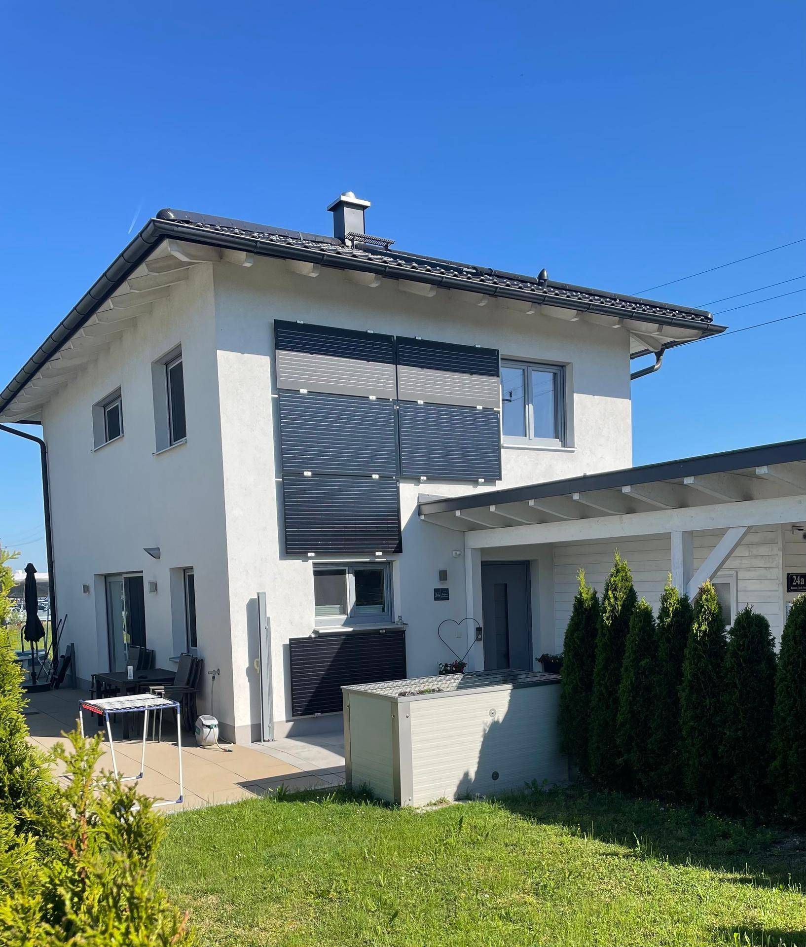 Modernes Einfamilienhaus mit weißer Fassade, Photovoltaikanlage und gepflegtem Vorgarten.