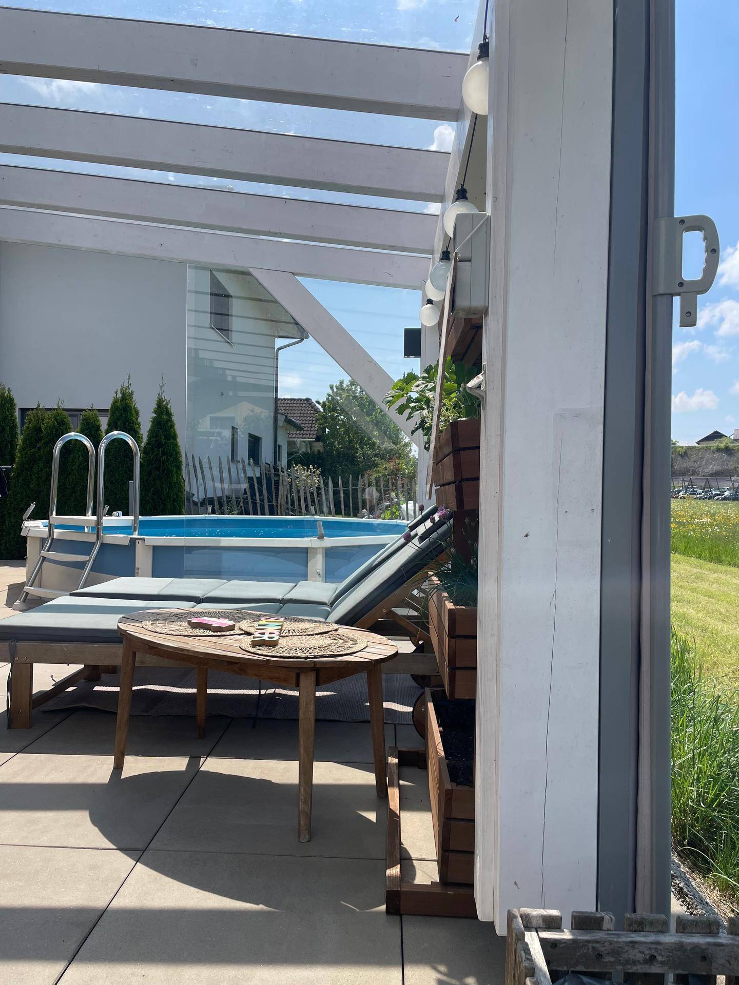 Teilansicht der überdachten Terrasse mit Pool im Hintergrund und Pflanzen.