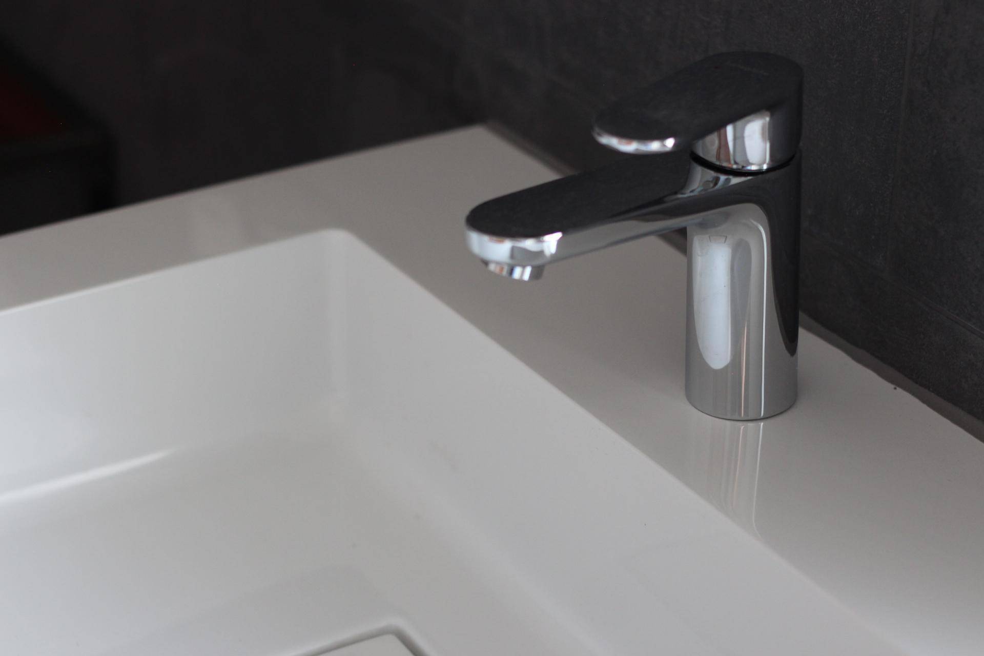 Nahaufnahme eines modernen Chromwasserhahns und eines weißen Waschbeckens im Badezimmer.