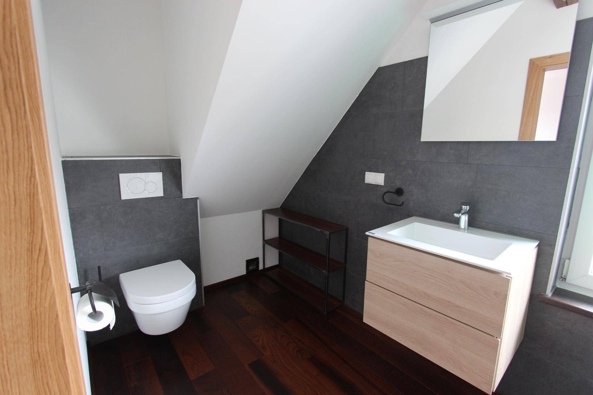 Modernes Badezimmer mit Waschtisch, Wand-WC und Spiegel unter der Dachschräge, ausgestattet mit dunklen Fliesen.