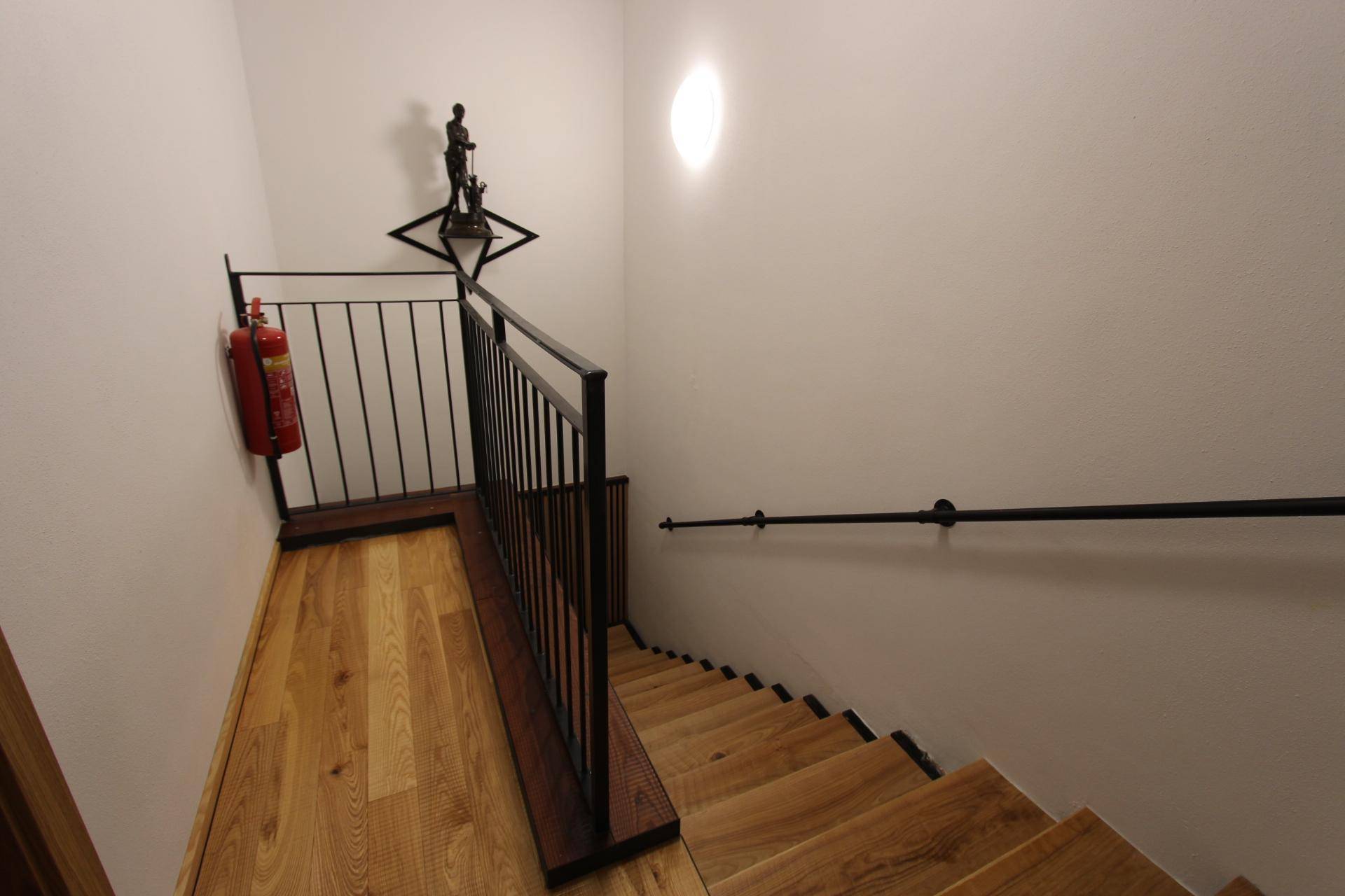 Holztreppe mit schwarzem Metallgeländer und Handlauf, führt in die obere Etage.