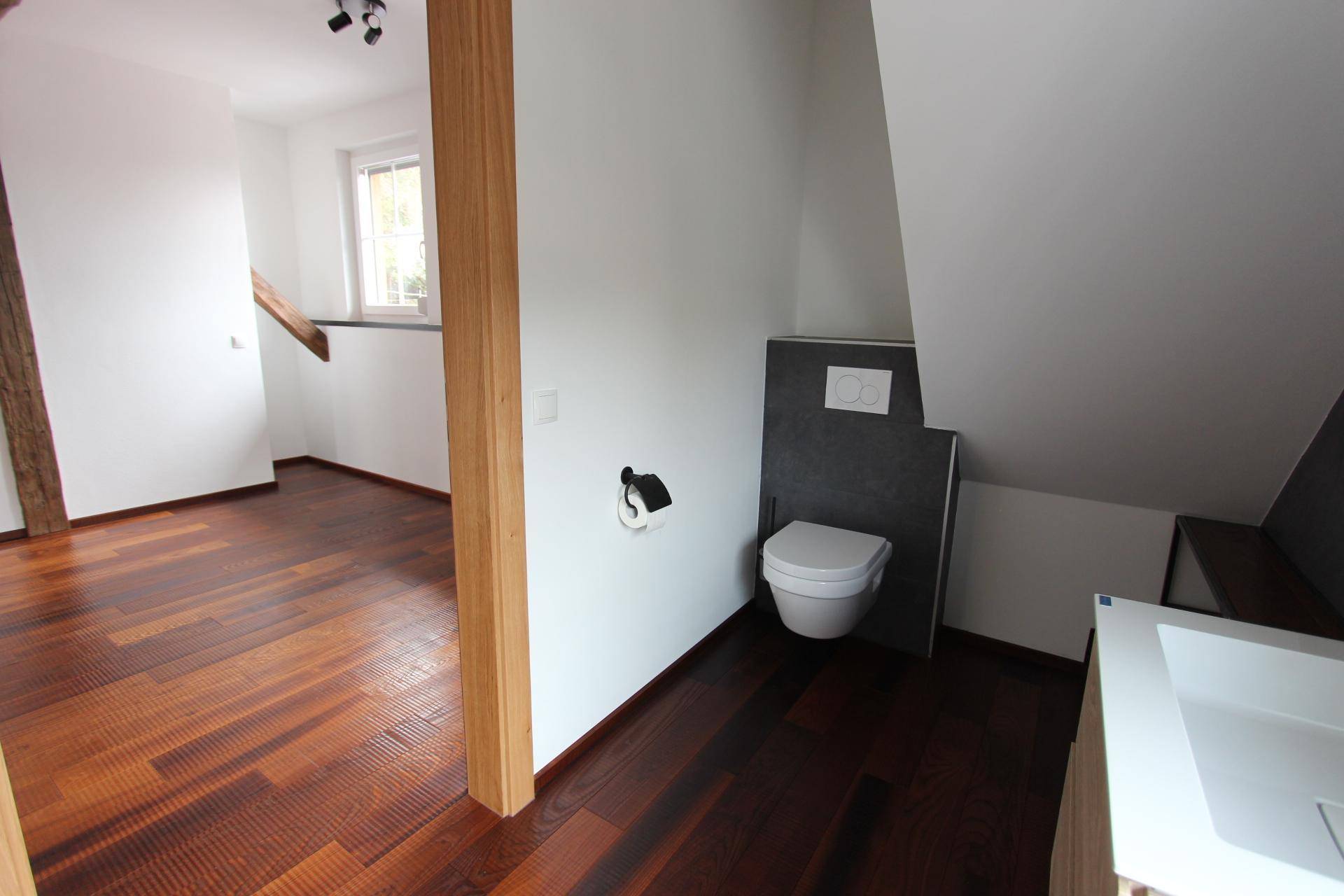 Blick in ein modernes Badezimmer mit Wand-WC, Waschtisch und dunklen Fliesen unter der Dachschräge.