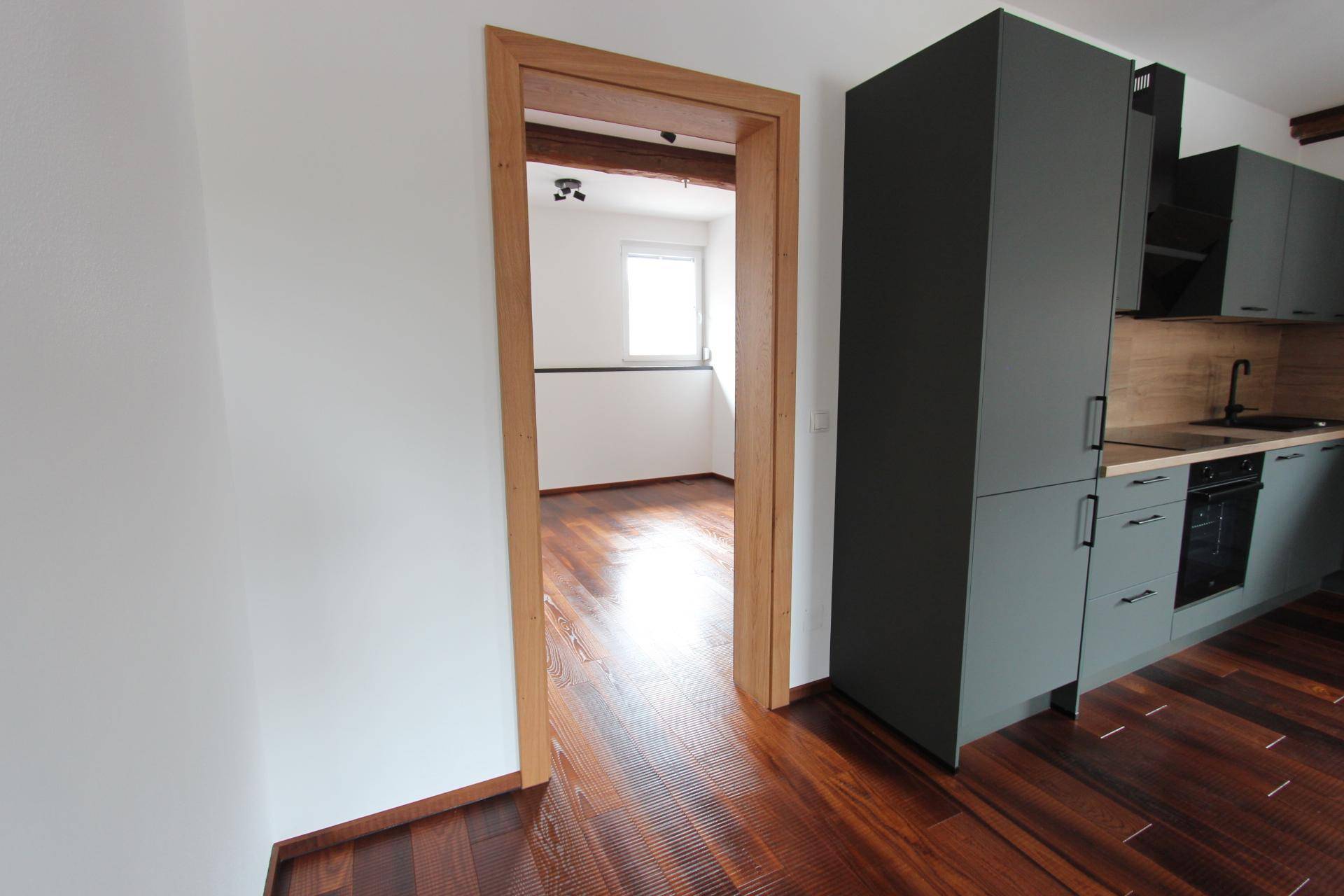 Blick durch eine Holztür in einen weiteren Raum mit dunklem Holzboden und natürlichem Lichteinfall.