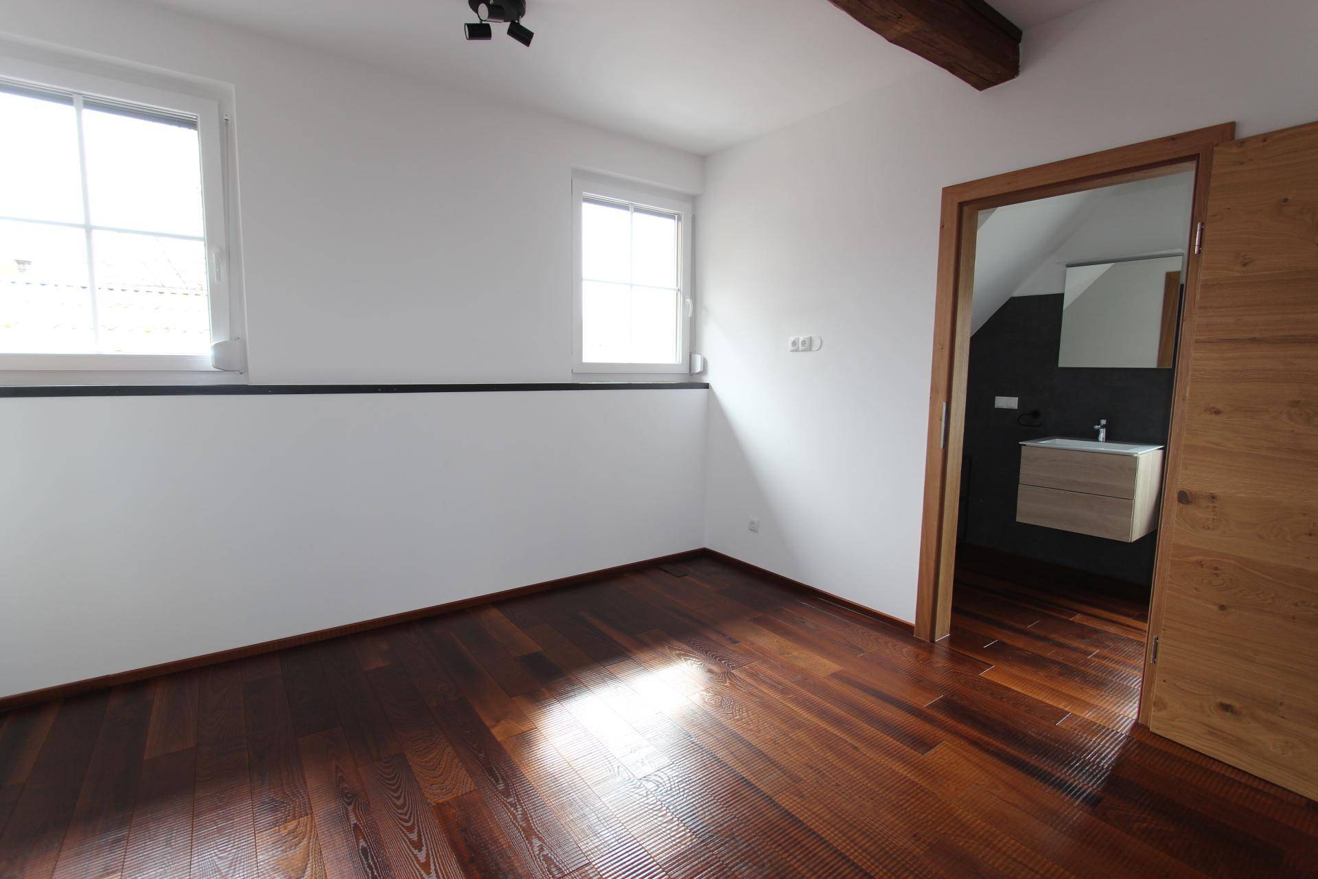Heller Raum mit dunklem Holzboden und Zugang zu einem modernen Badezimmer mit Waschtisch.