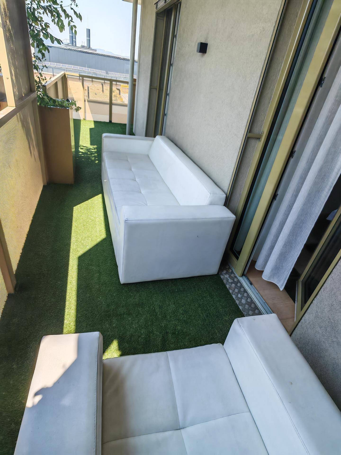 Langer Balkon mit Kunstrasen und bequemen weißen Outdoor-Sofas zum Entspannen.