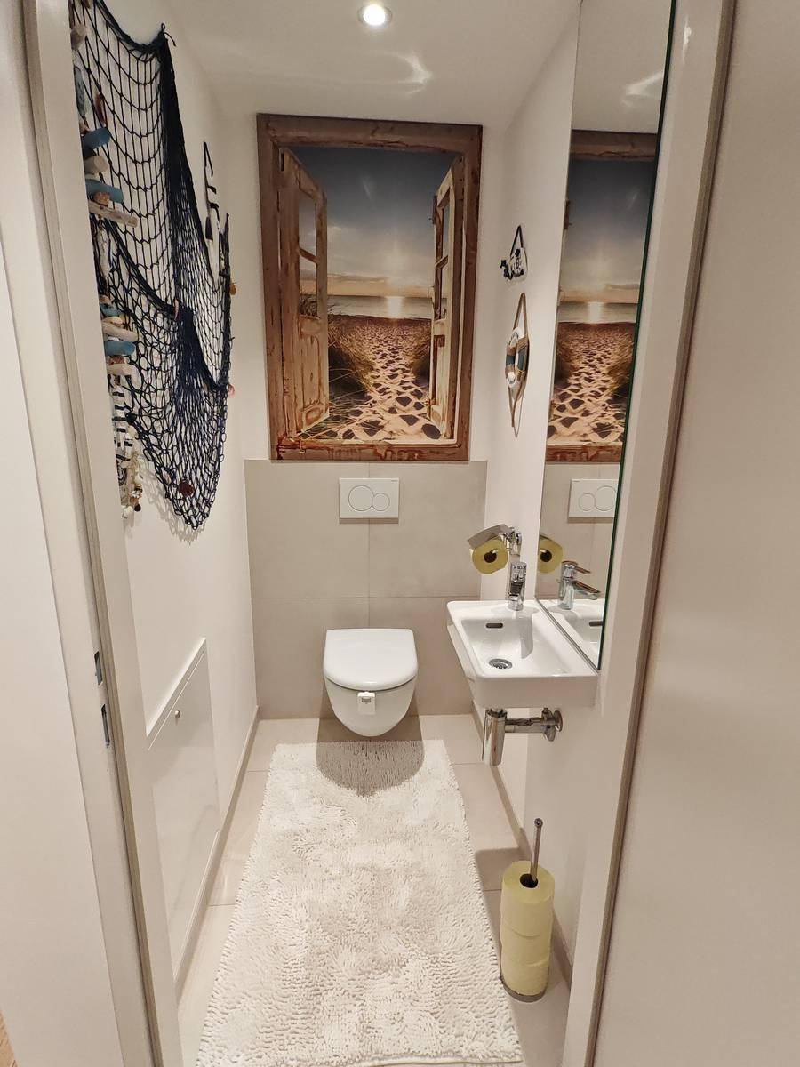 Kleines Gäste-WC mit wandhängendem WC, Handwaschbecken und maritimer Dekoration.