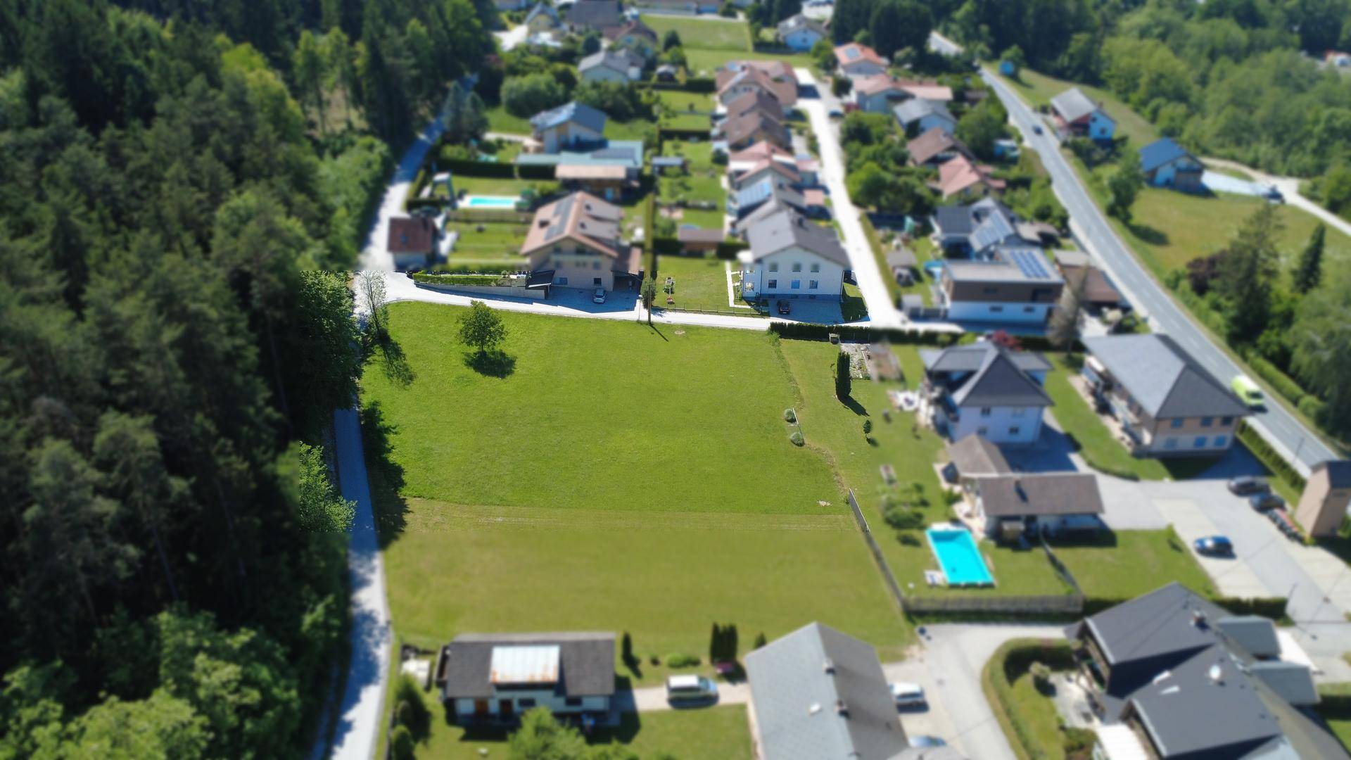 Umfassende Luftaufnahme eines großen Baugrundstücks in einer Siedlung mit viel Grün und Wald.