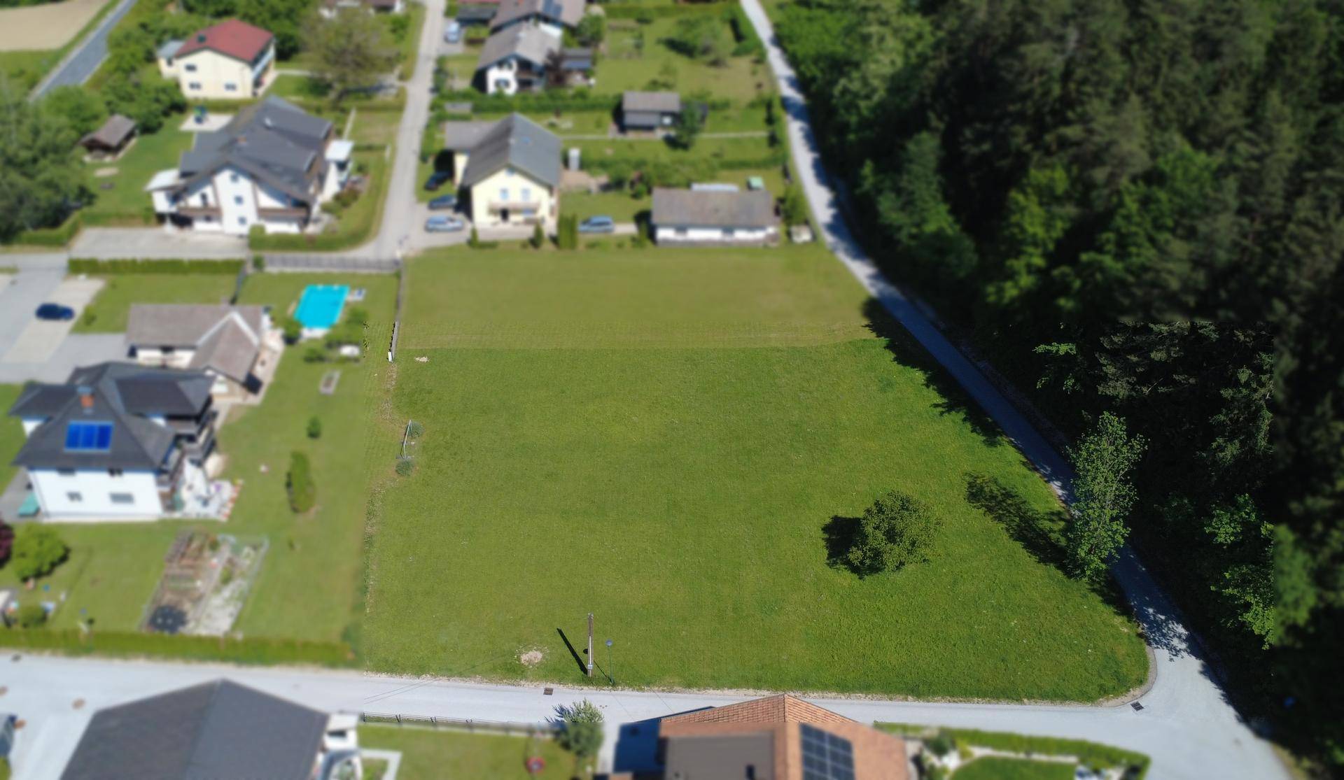 Weitläufige Luftaufnahme eines grünen Grundstücks mit umliegenden Wohnhäusern und Waldrand.
