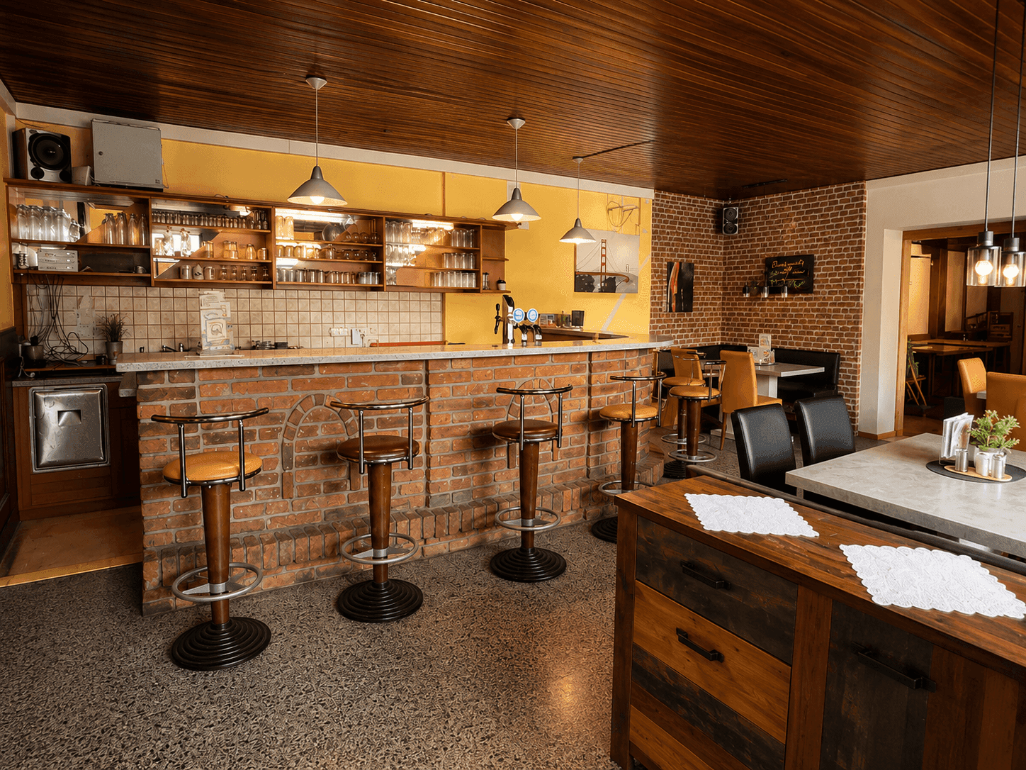 Gemütlicher Barbereich mit Ziegeltheke, Hockern und Holzdecke in einem Restaurant.