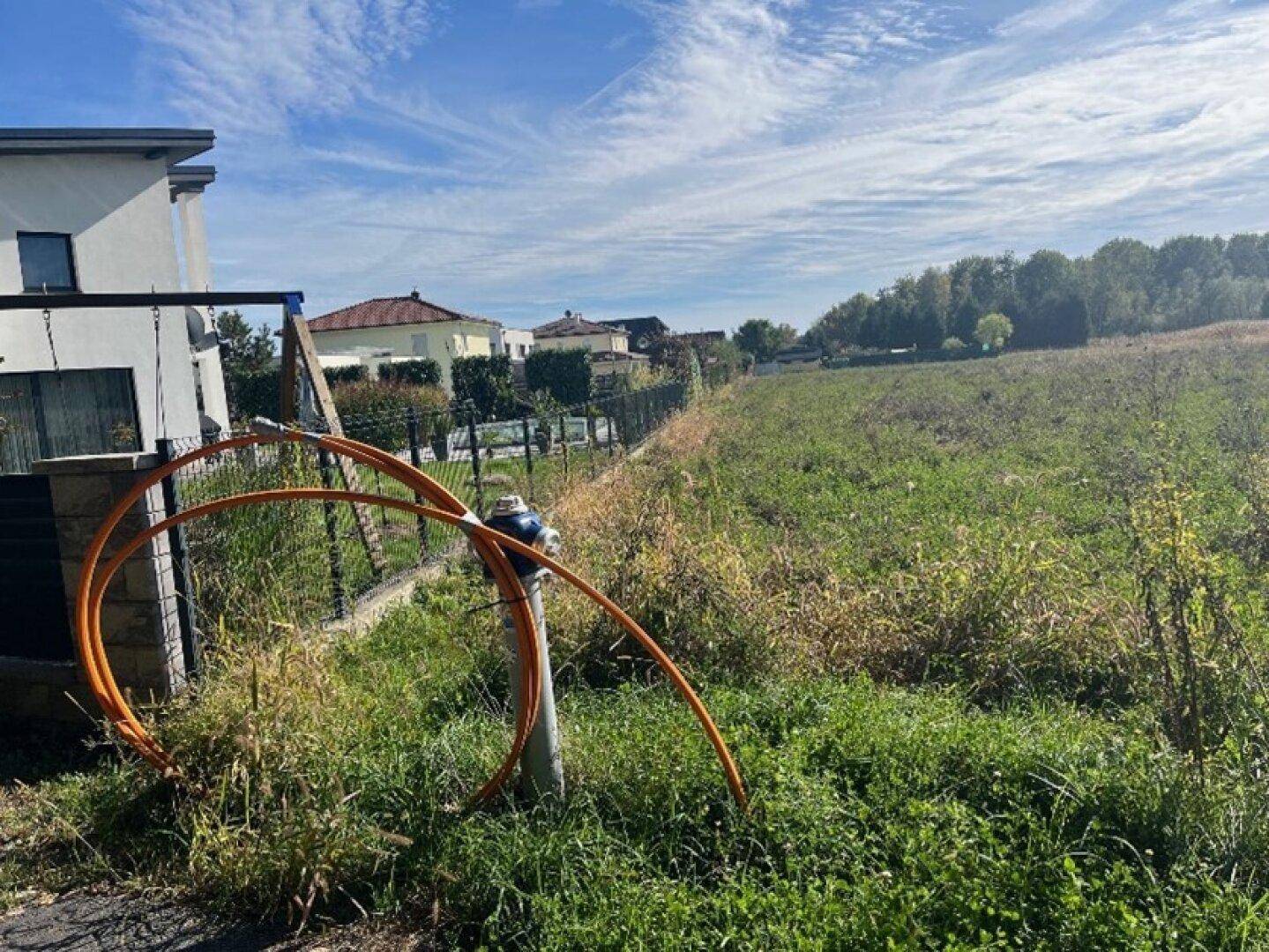 Blick über ein Feld mit einem modernen Haus im Hintergrund und orangefarbenen Rohren im Vordergrund.