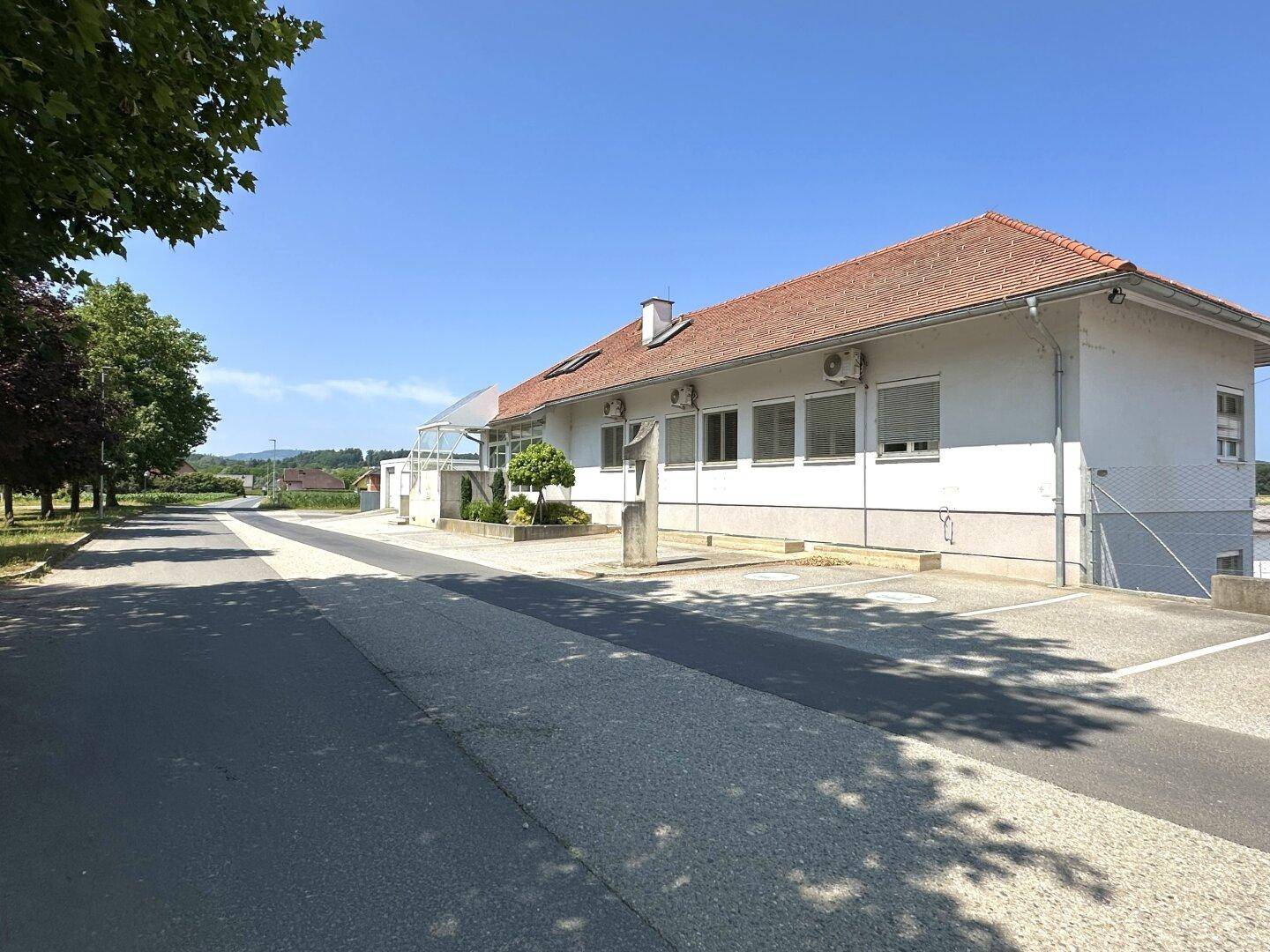 Weitläufige Außenansicht des Gebäudes mit rotem Ziegeldach, umgeben von Bäumen und einer Zufahrtsstraße.