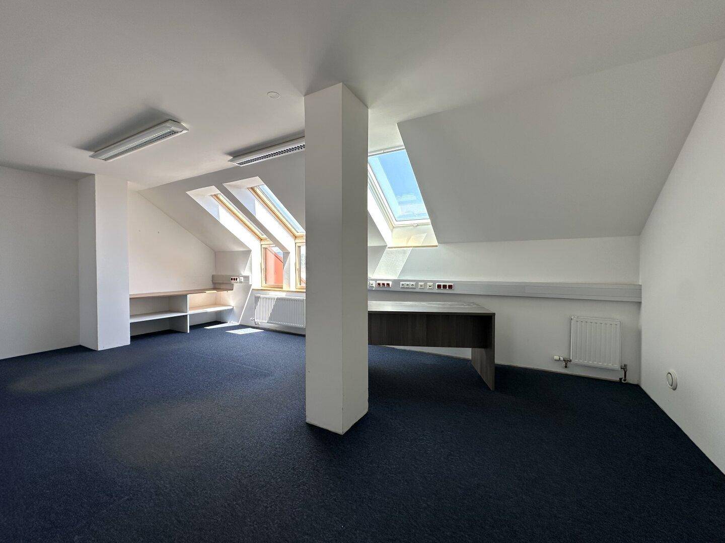 Geräumiges Büro im Dachgeschoss mit Teppichboden, Dachfenstern und einem großen Schreibtisch.