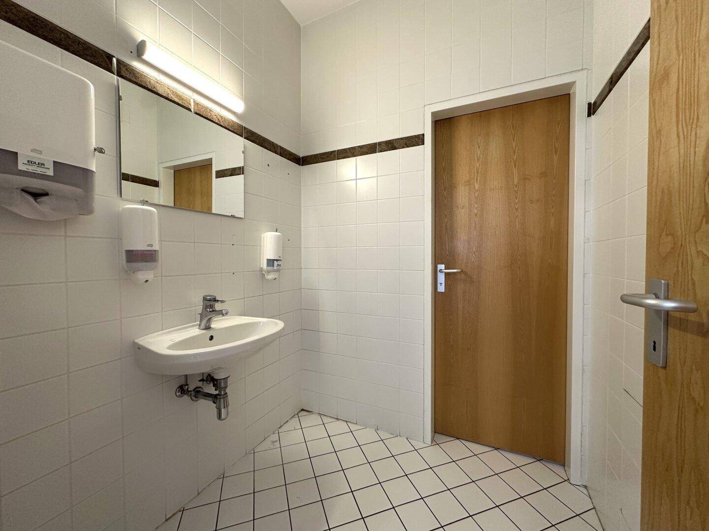 Gefliestes Badezimmer mit Waschbecken, Spiegel und zwei Holztüren, funktional und hell.