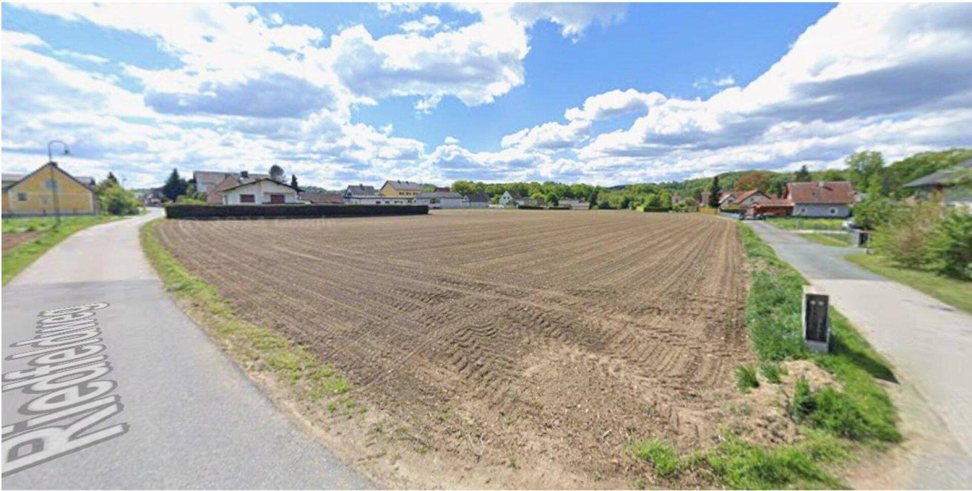 Weitläufiges Ackerland an einer Landstraße mit Blick auf die umliegende Wohnbebauung.