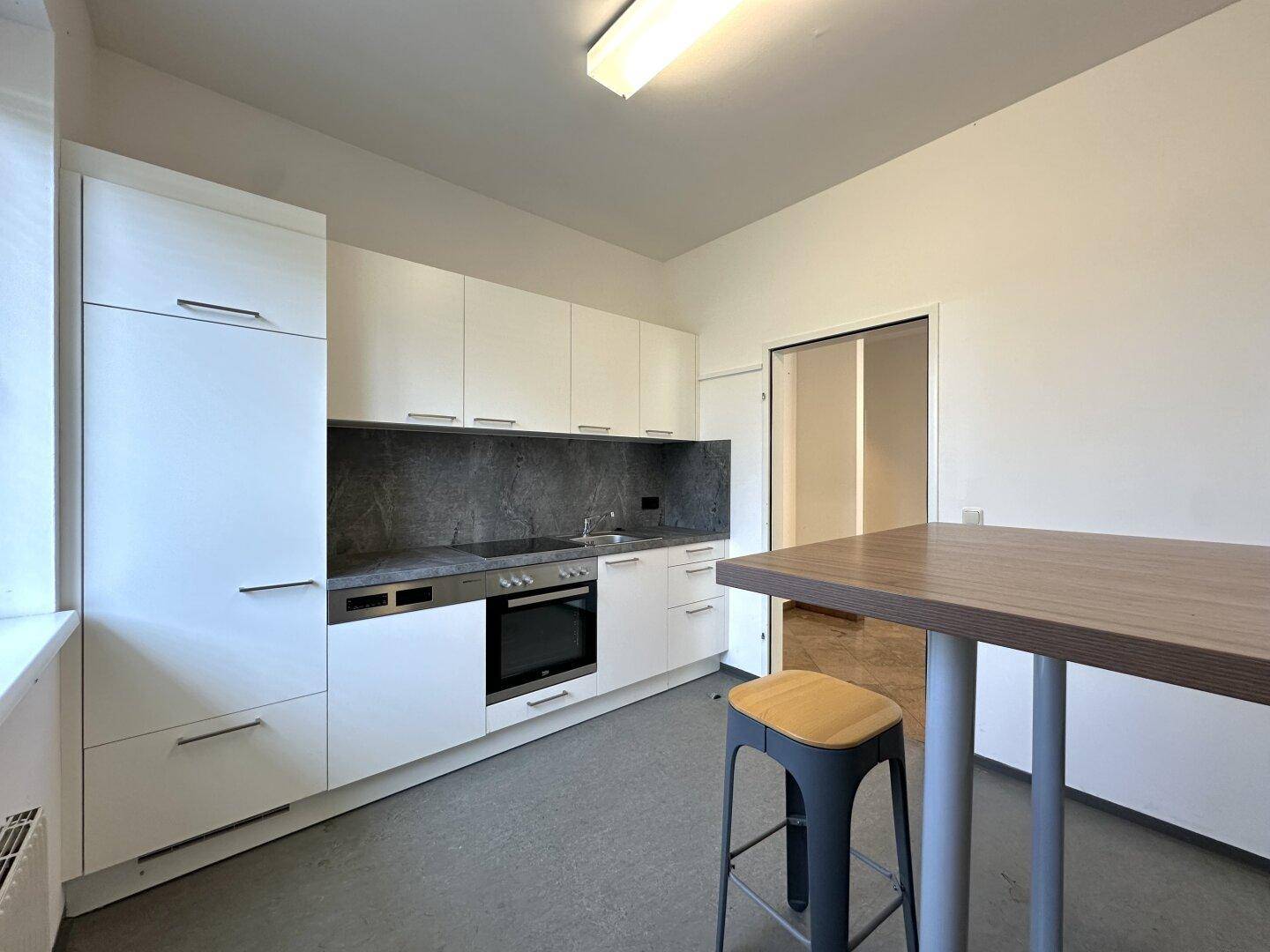 Moderne Einbauküche mit weißen Schränken, dunkler Arbeitsplatte und einem praktischen Bartisch.