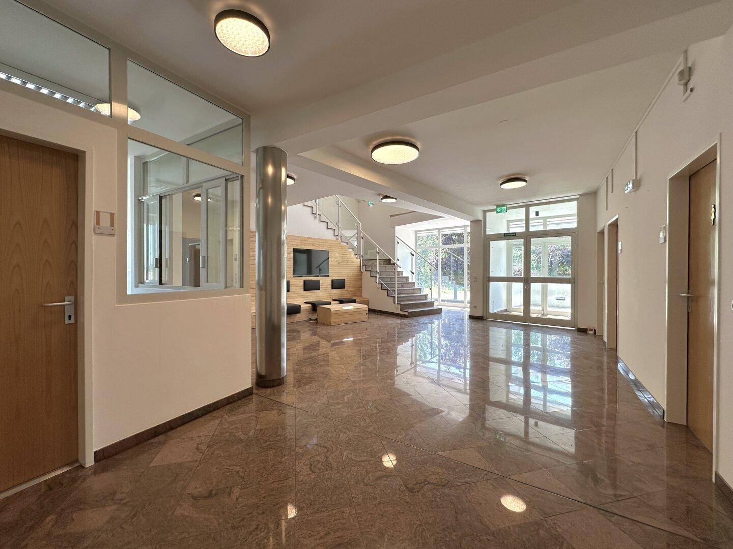 Geräumiger Eingangsbereich mit Marmorboden, moderner Treppe und viel Tageslicht durch große Fenster.
