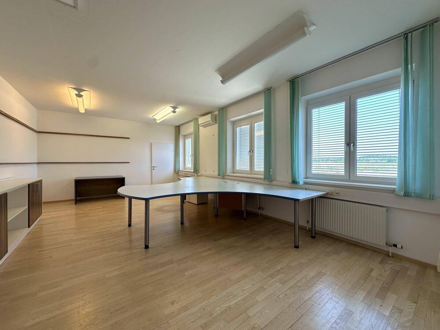 Großes Büro mit Holzfußboden, langen Fenstern und einem geschwungenen Schreibtisch für mehrere Arbeitsplätze.