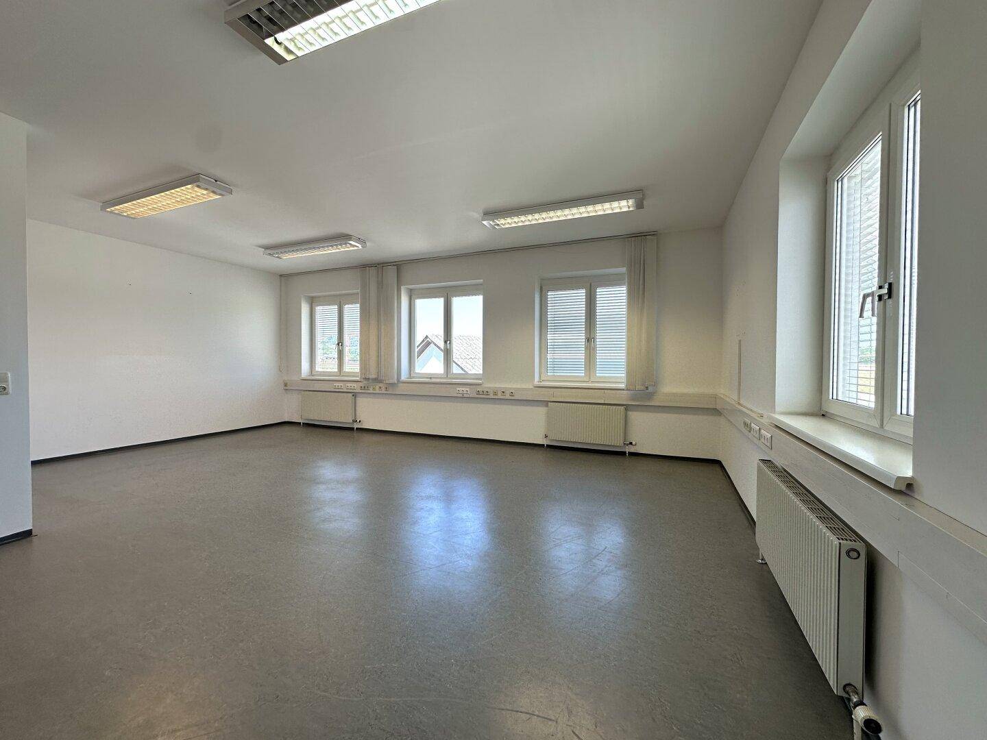 Geräumiges Büro mit grauem Vinylboden und mehreren Fenstern, die viel Tageslicht hereinlassen.