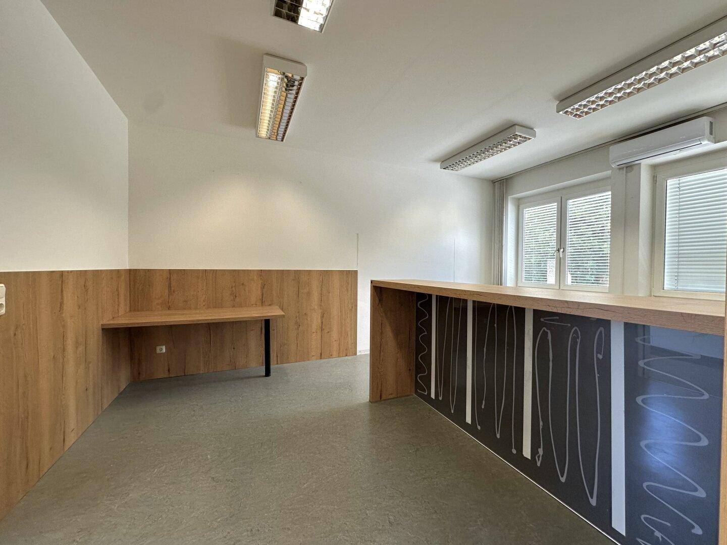 Büro mit grauem Vinylboden, Holzwandverkleidung und einem langen Arbeitstisch für kreative Aufgaben.