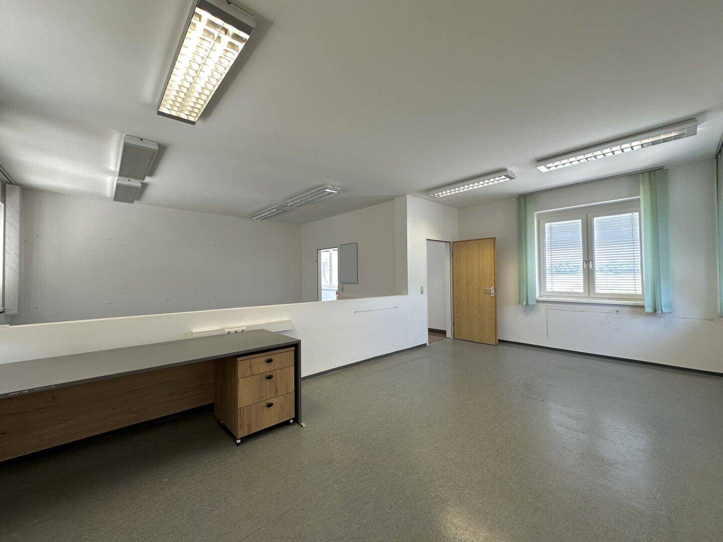 Helles Büro mit grauem Vinylboden, Fenstern und einem Schreibtisch mit Schubladen für Stauraum.